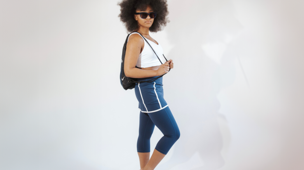 A woman wearing a white tank top and blue leggings. She is showcasing skirted capri leggings, a trendy summer fashion.