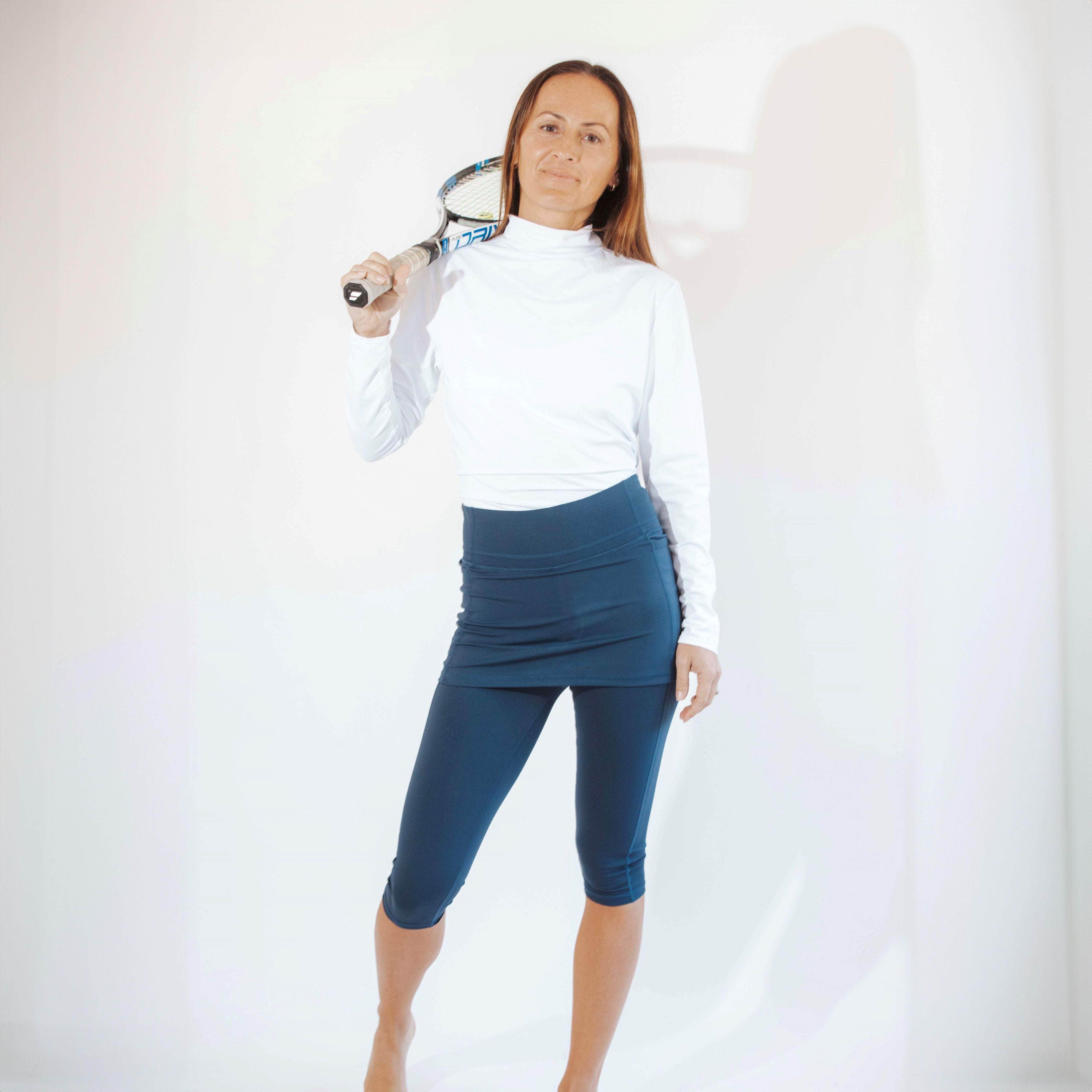 Model wearing pretty blue capris length skirted leggings with white athletic turtleneck and tennis racket in hand.