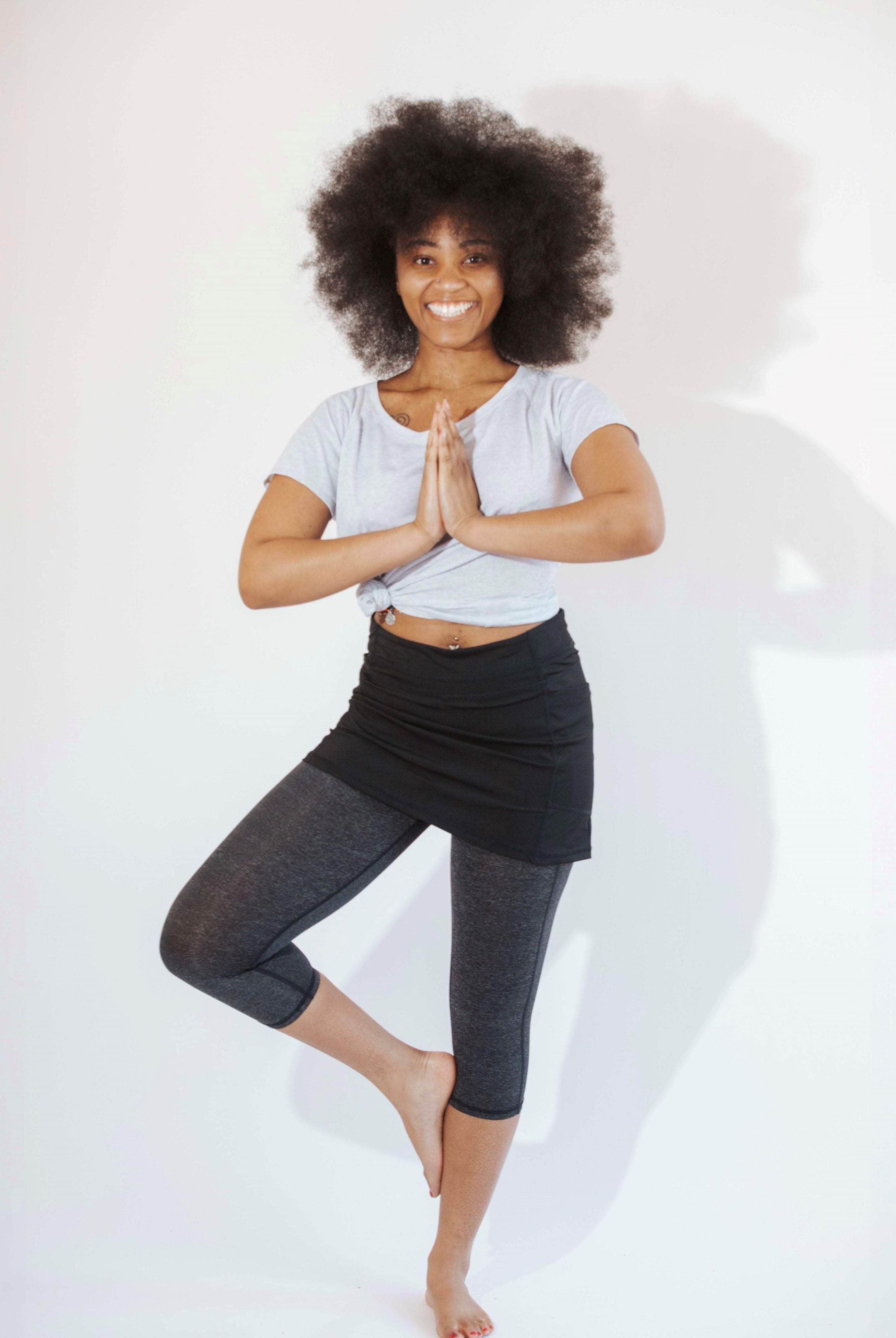 One piece black skirt with heather grey capris length leggings. Model is standing in yoga pose on one foot with hands together at her chest.