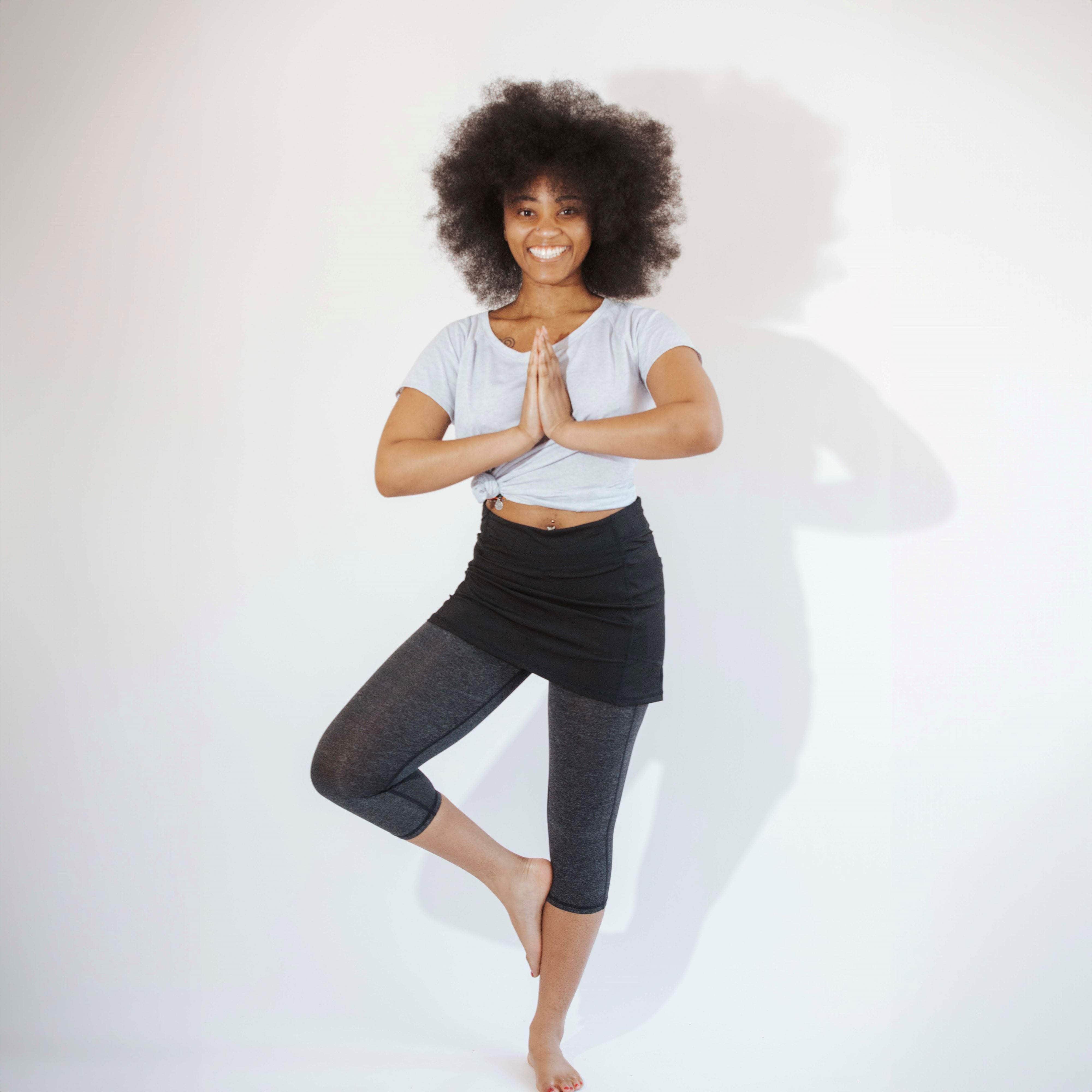 One piece black skirt with heather grey capris length leggings. Model is standing in yoga pose on one foot with hands together at her chest.