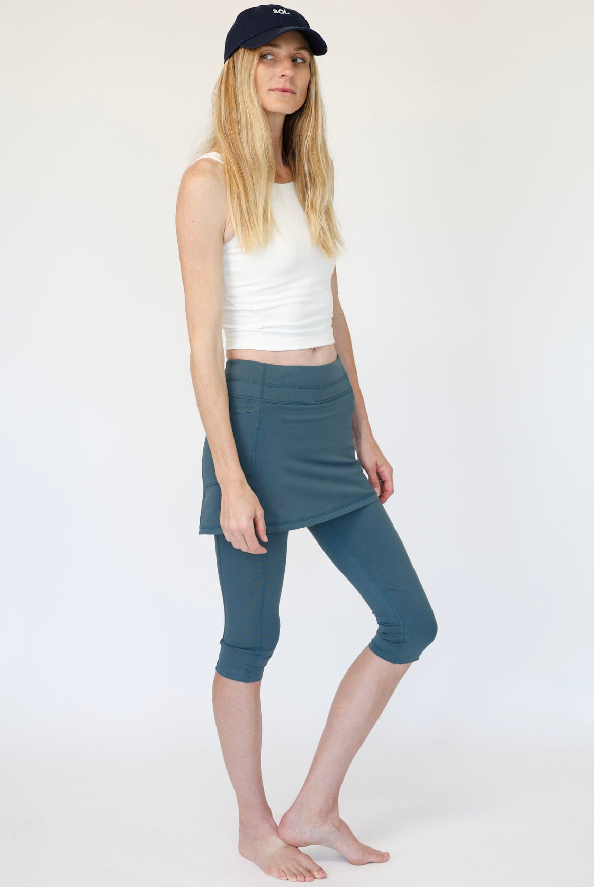 Woman wearing a white tank top and blue capri pants on a white background