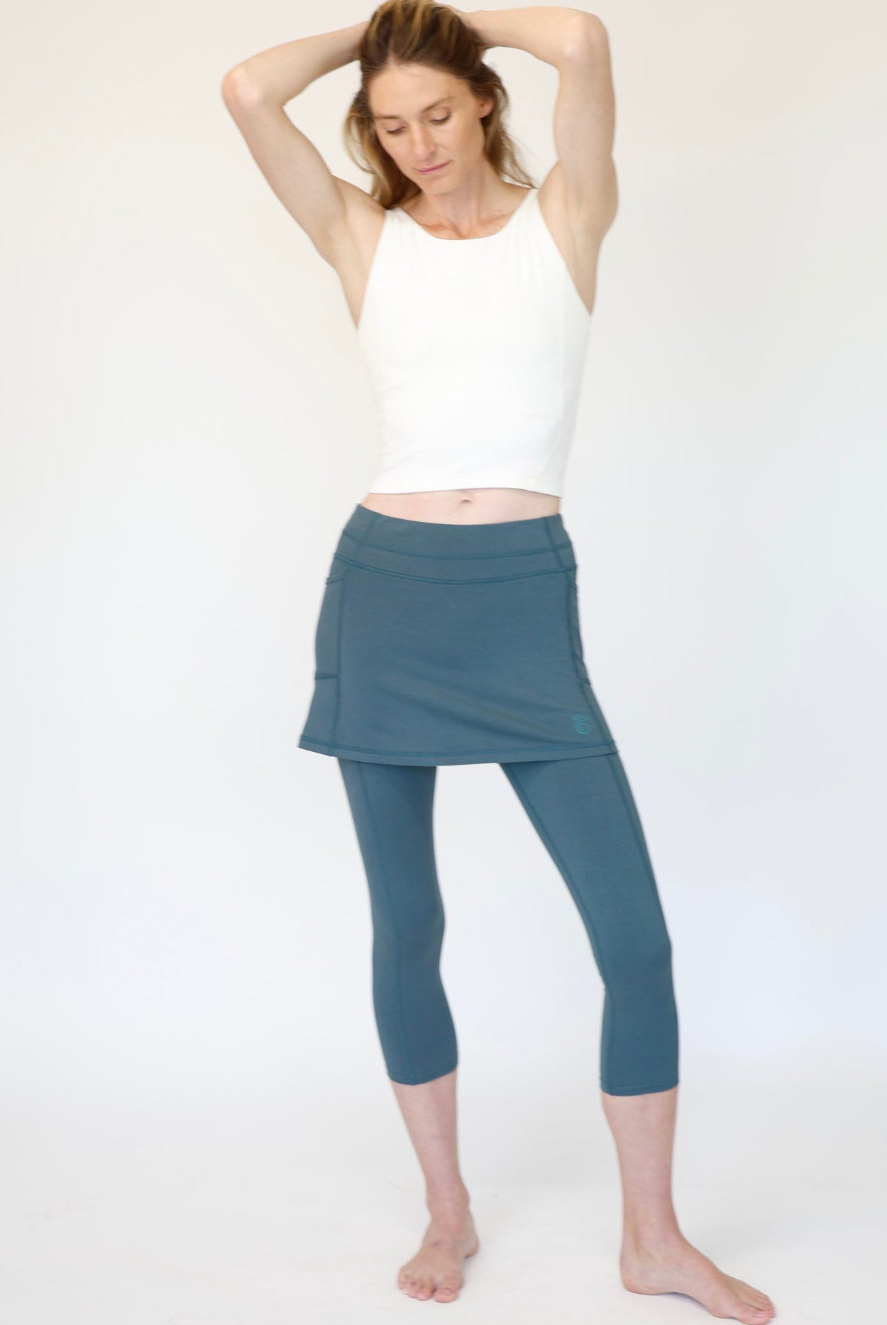 Woman wearing a white tank top and blue skirted leggings on a white background