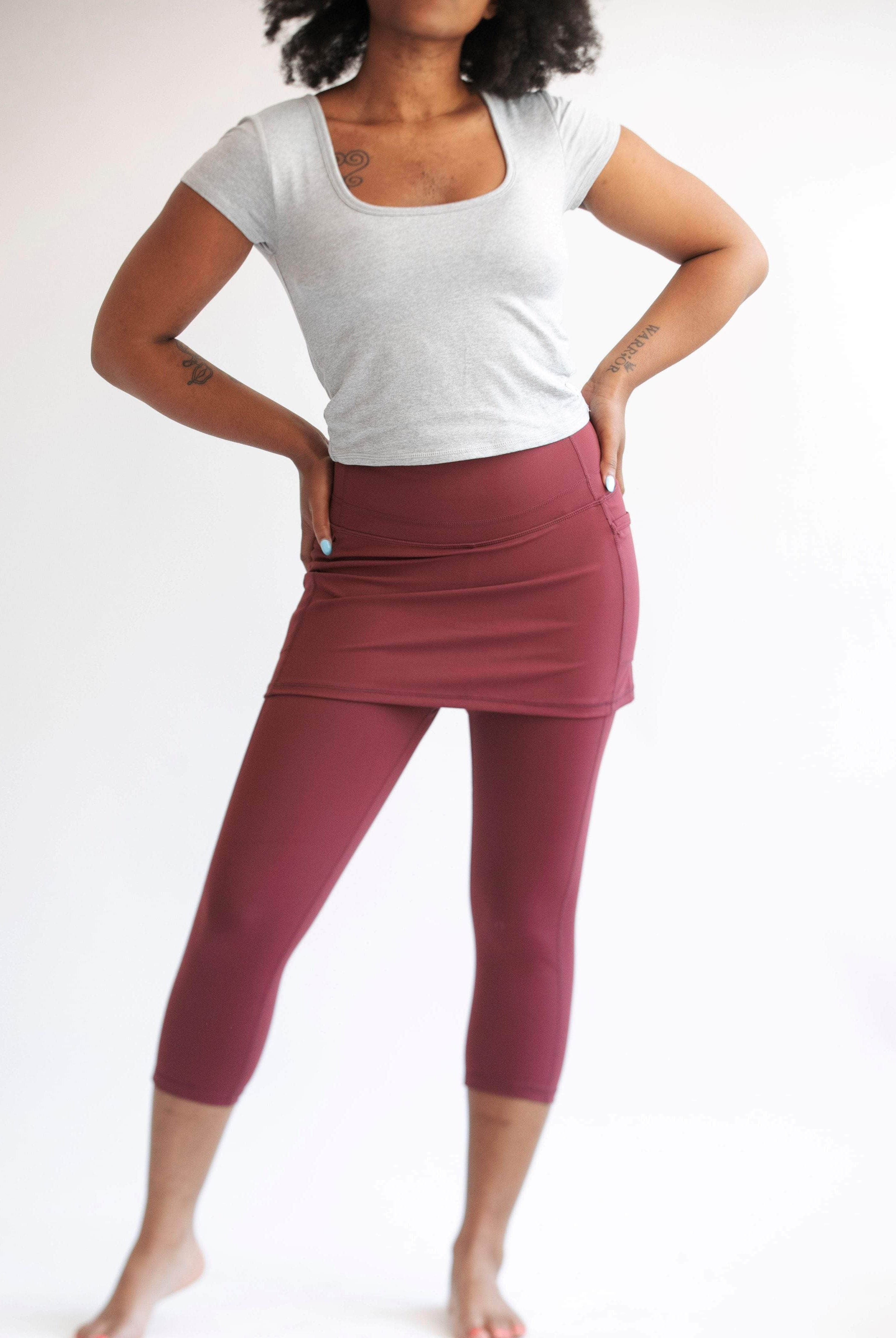 Studio shot of model wearing capris length cranberry colored skirted leggings with grey t-shirt.
