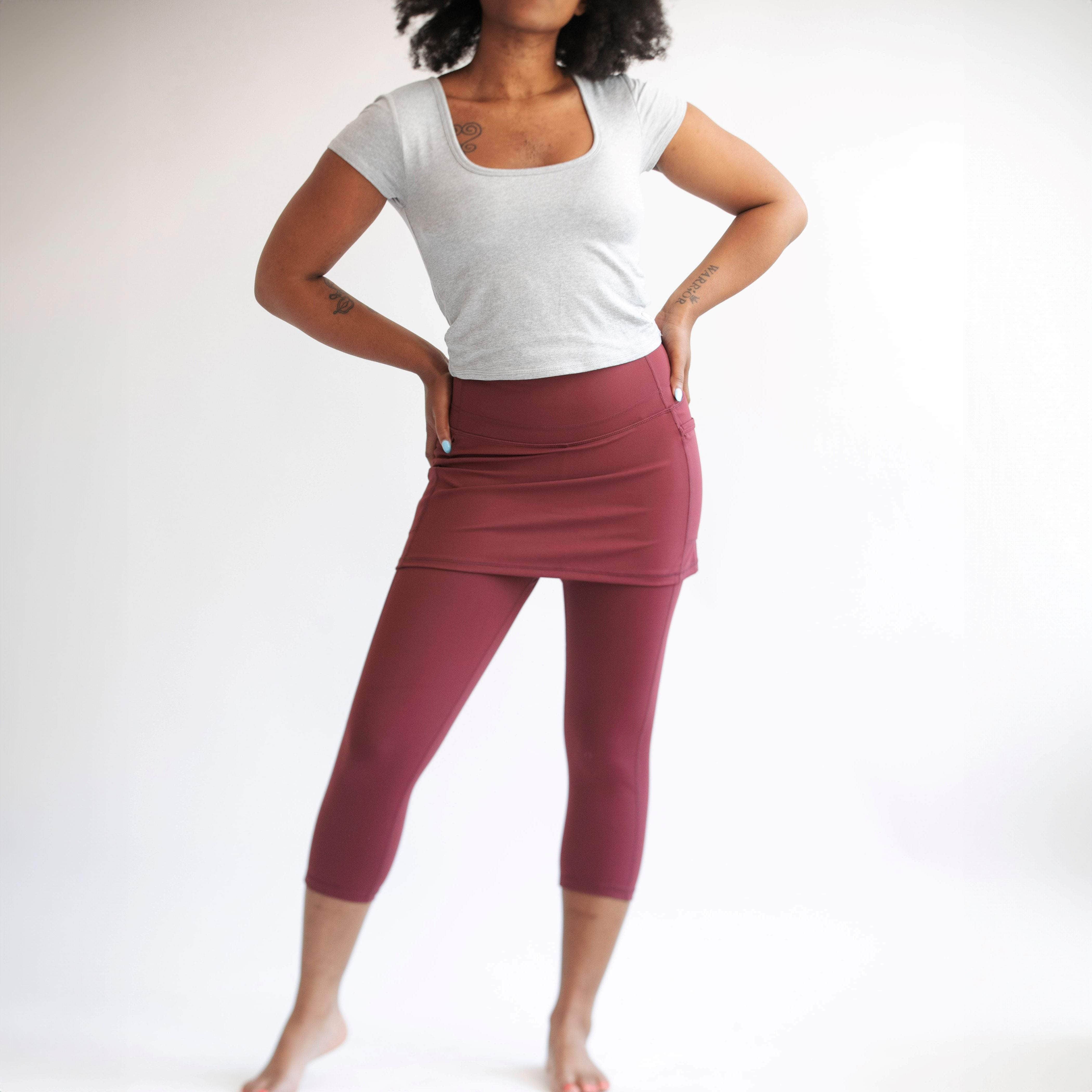 Studio shot of model wearing capris length cranberry colored skirted leggings with grey t-shirt.