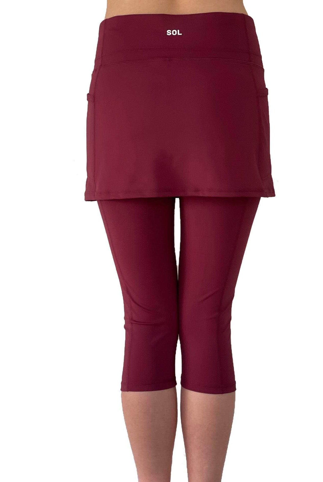 Studio shot of model from waist down wearing capris length cranberry colored skirted leggings, rear view.