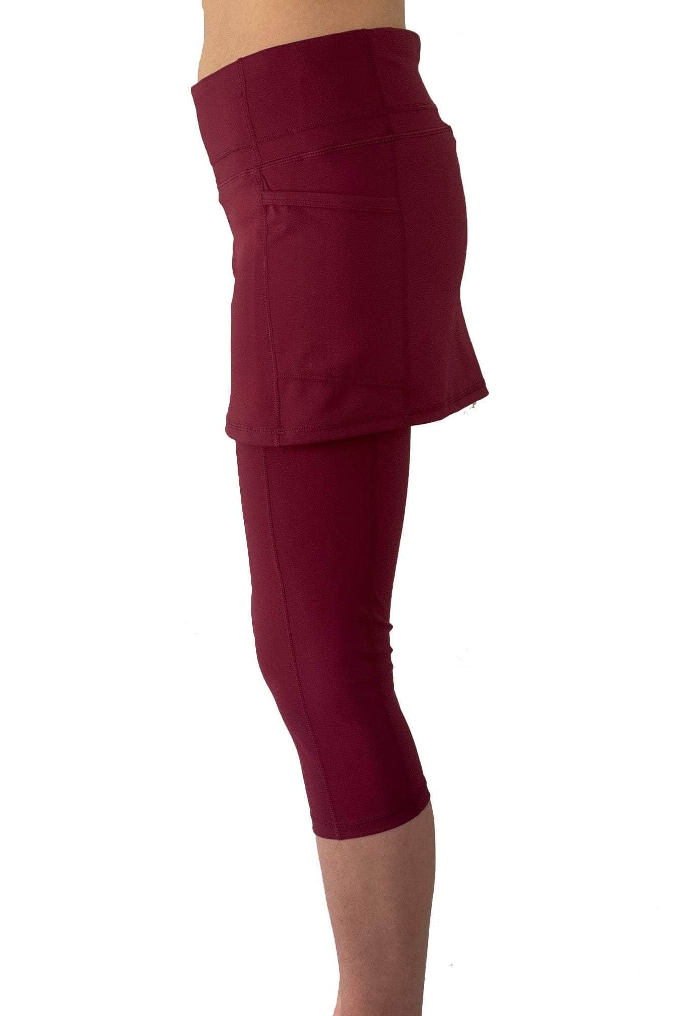 Studio shot of model from waist down wearing capris length cranberry colored skirted leggings, side view.