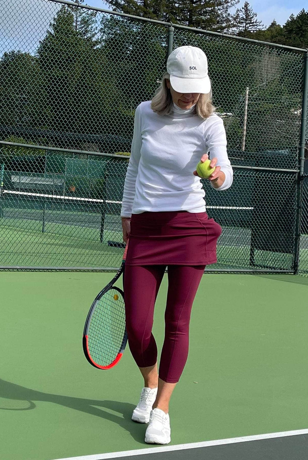 Woman in pretty dark red skirted leggings on tennis court about to serve.