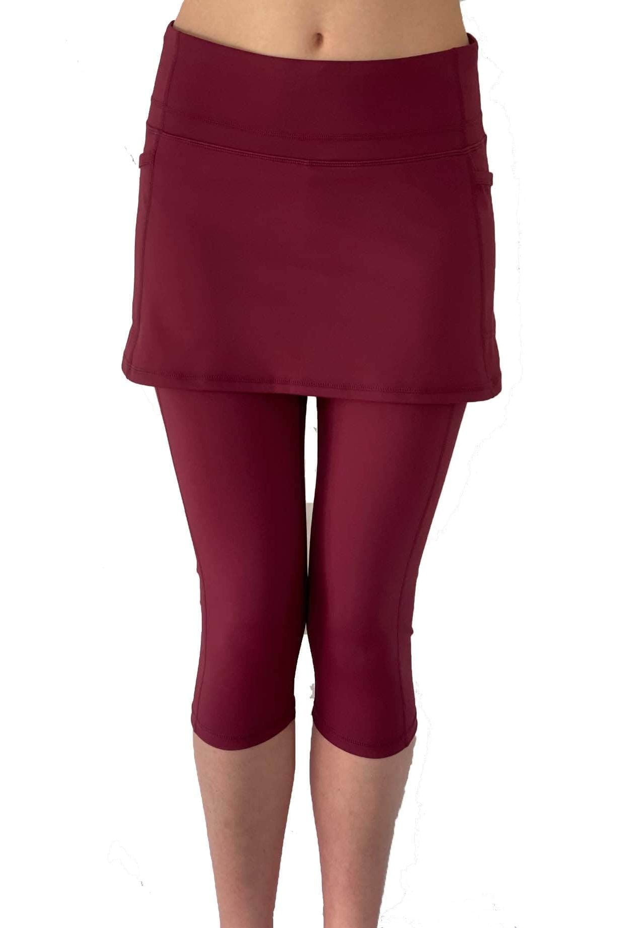 Studio shot of model from waist down wearing capris length cranberry colored skirted leggings, front view.