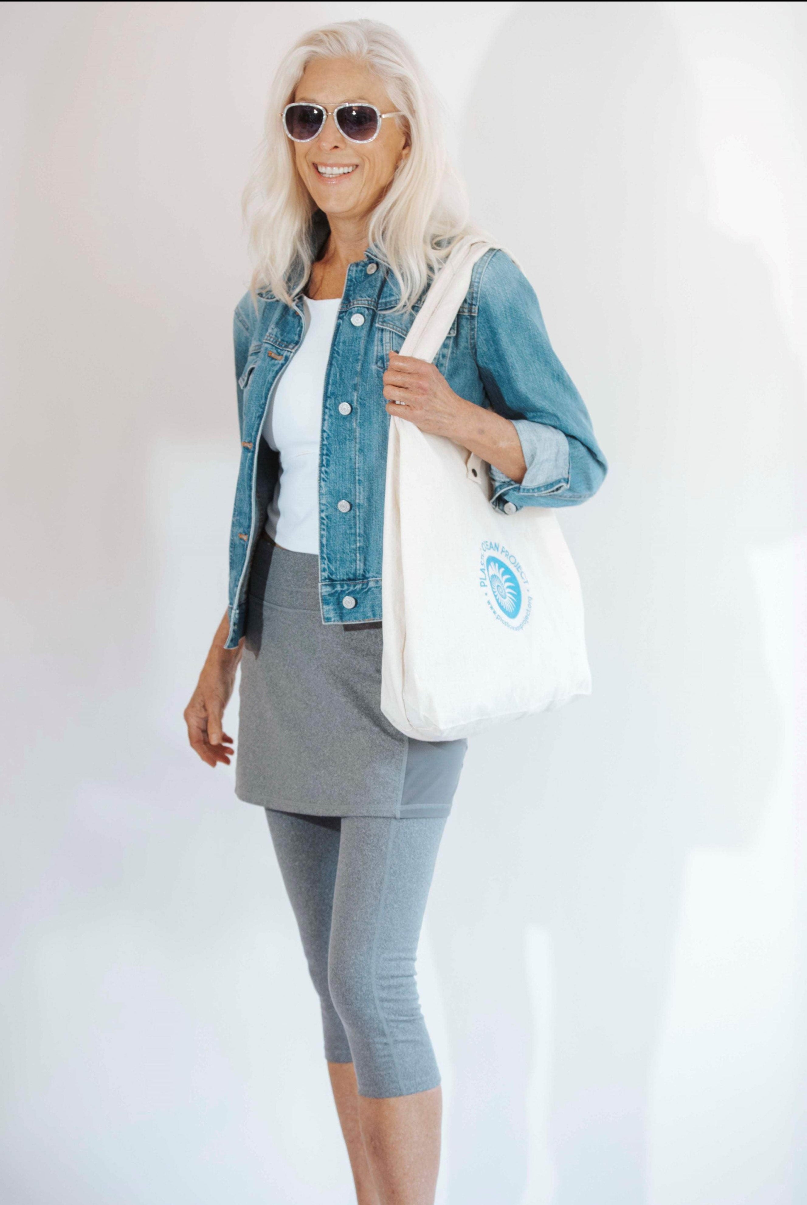 Side view of pretty older model wearing 3/4 length heather grey leggings with attached skirt and white top and jean jacket.