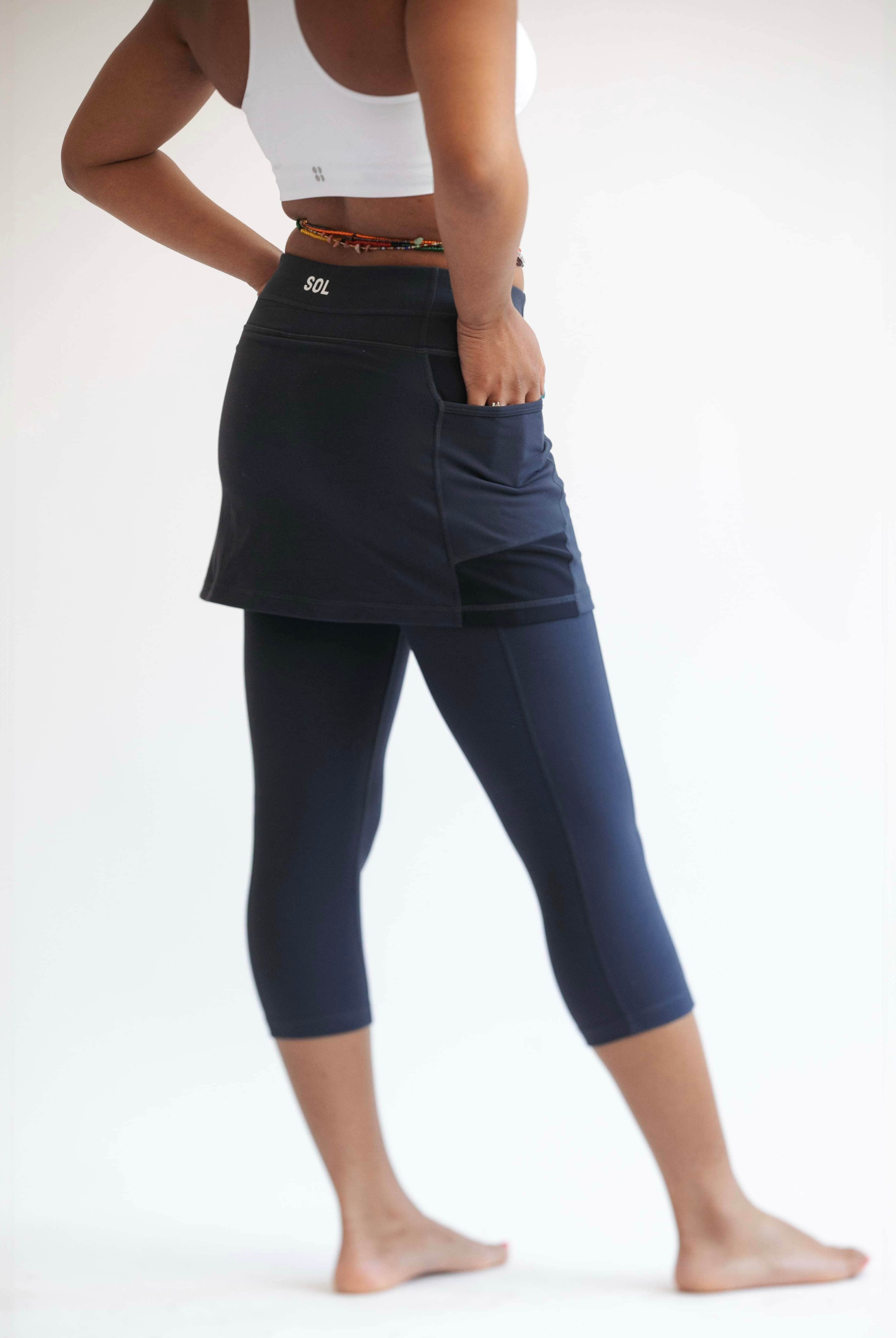 Rear shot of model wearing midnight dark blue leggings with attached skirt and white sports bra on top..