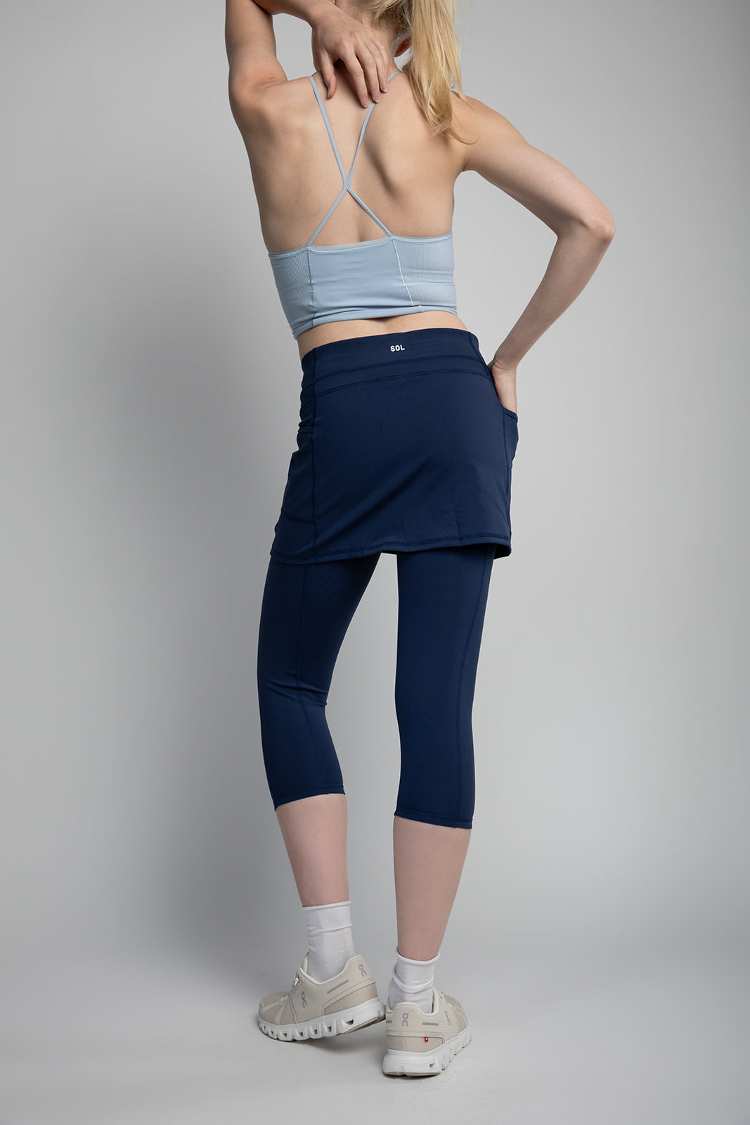 Studio shot of model wearing dark blue capris length leggings with attached skirt.