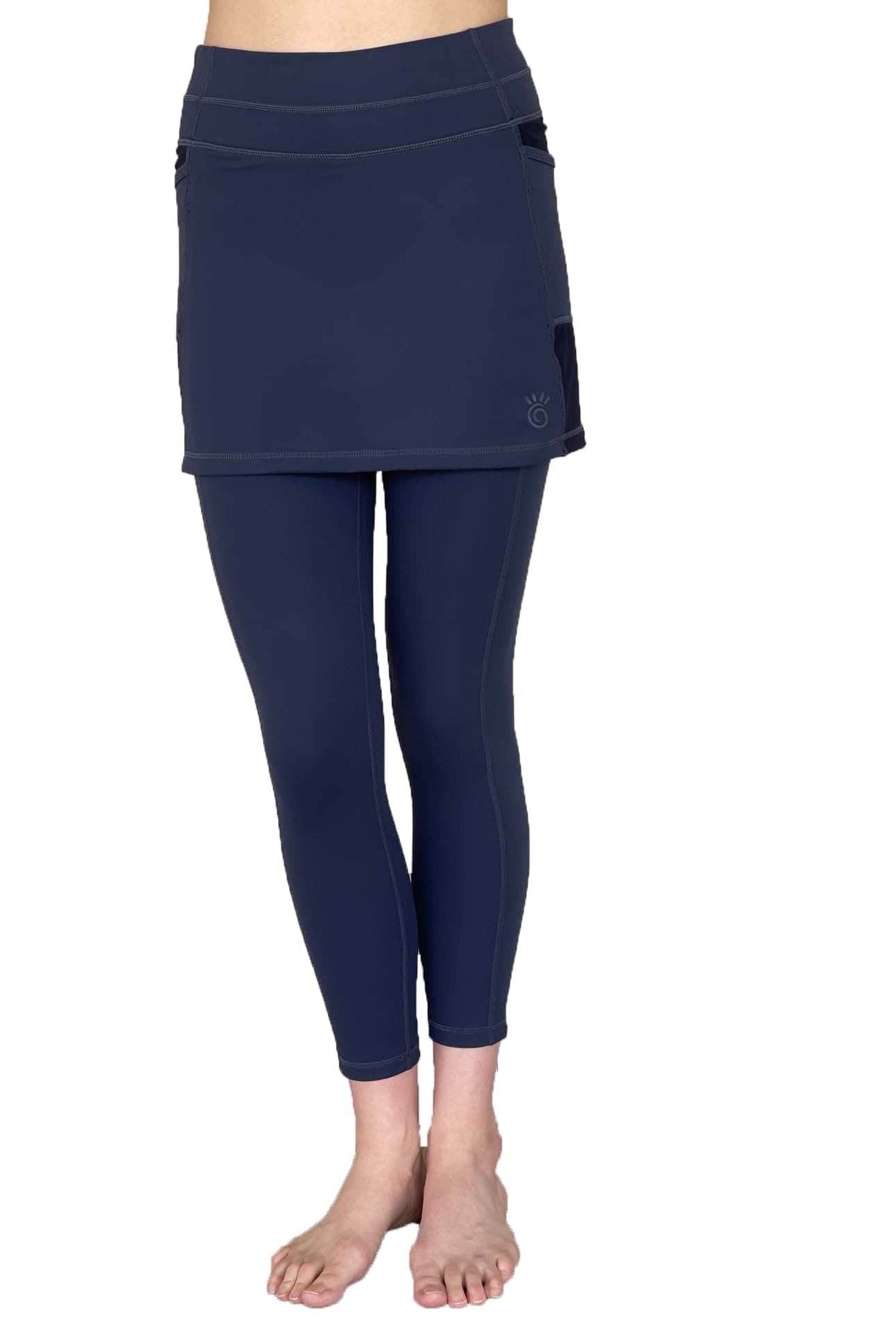 Woman wearing dark blue 7/8th legging length skirted leggings from waist down with white background from front view.