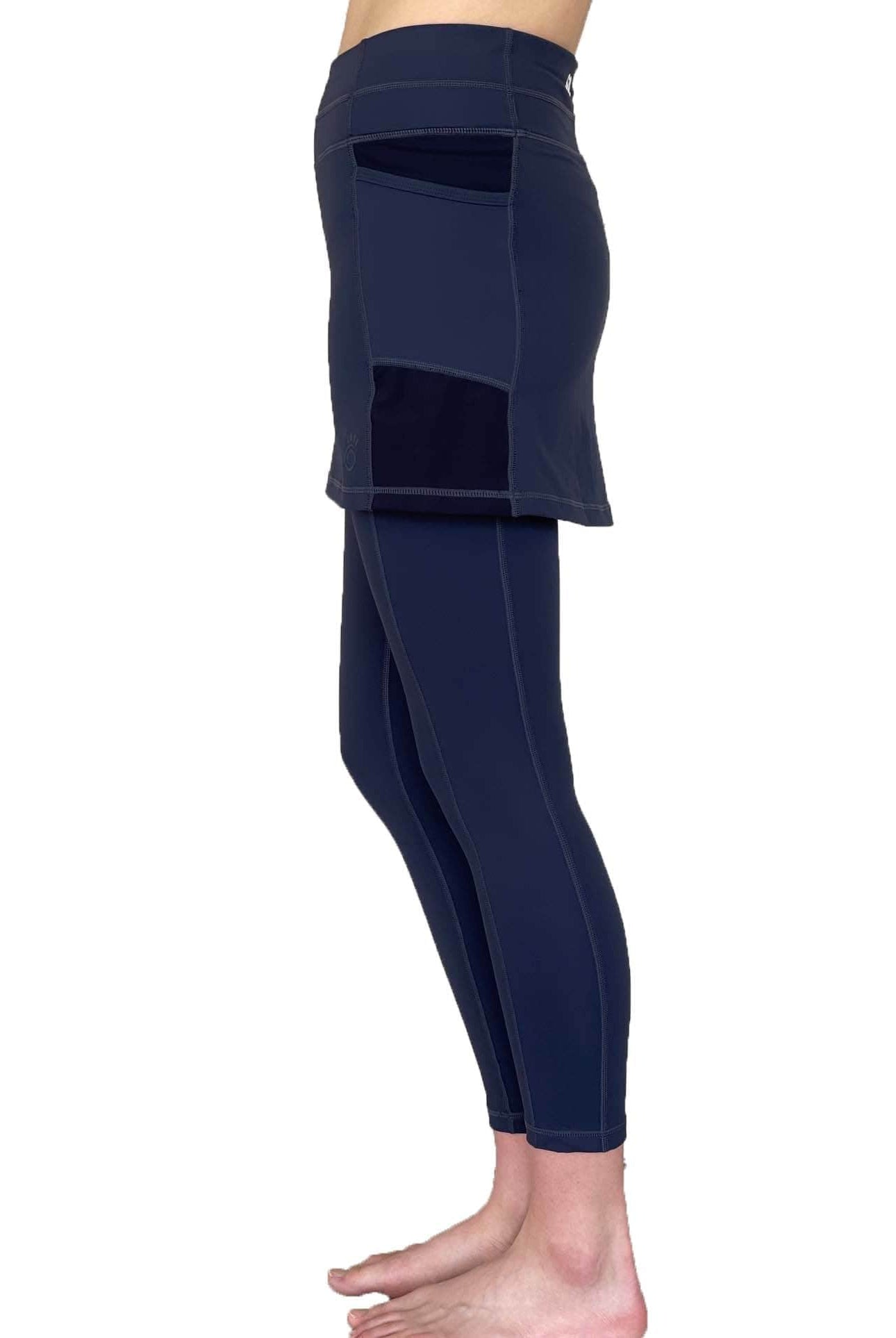 Woman wearing dark blue 7/8th legging length skirted leggings from waist down with white background from side view.