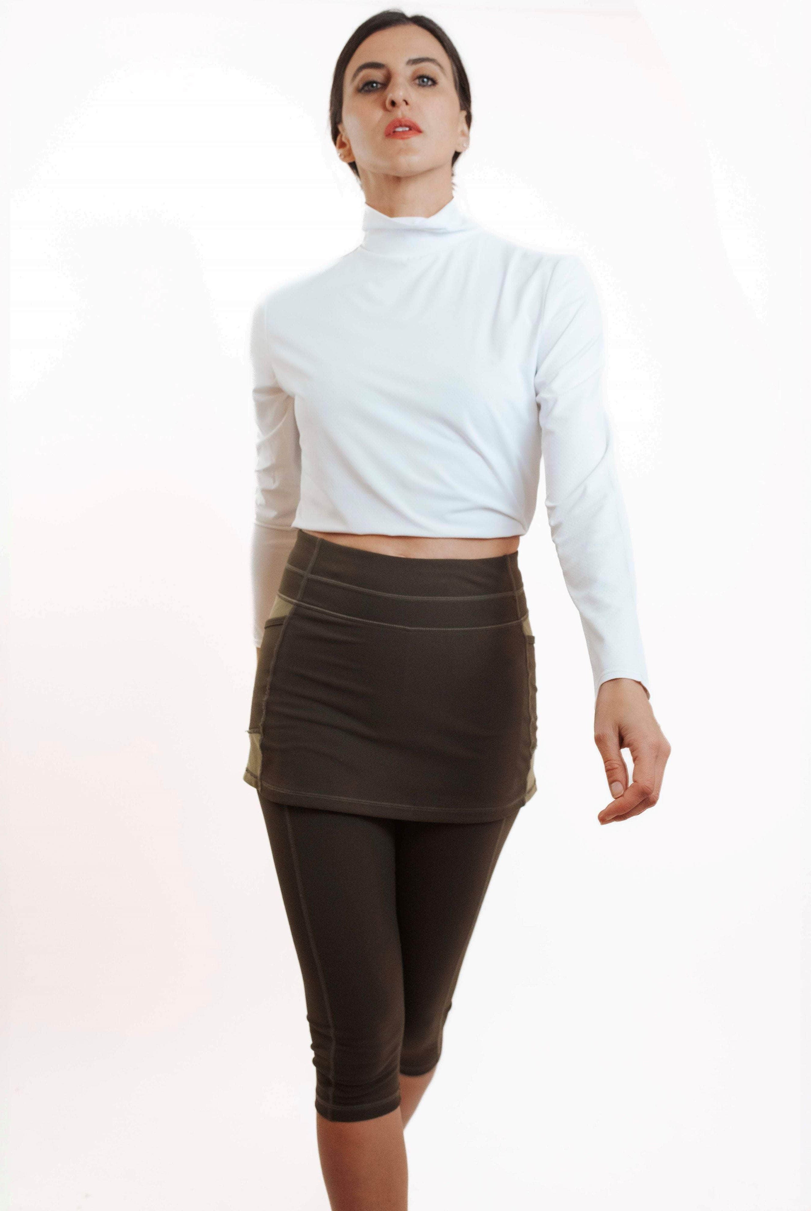 Studio shot of model wearing olive leggings with attached olive skirt and white turtleneck athletic top.