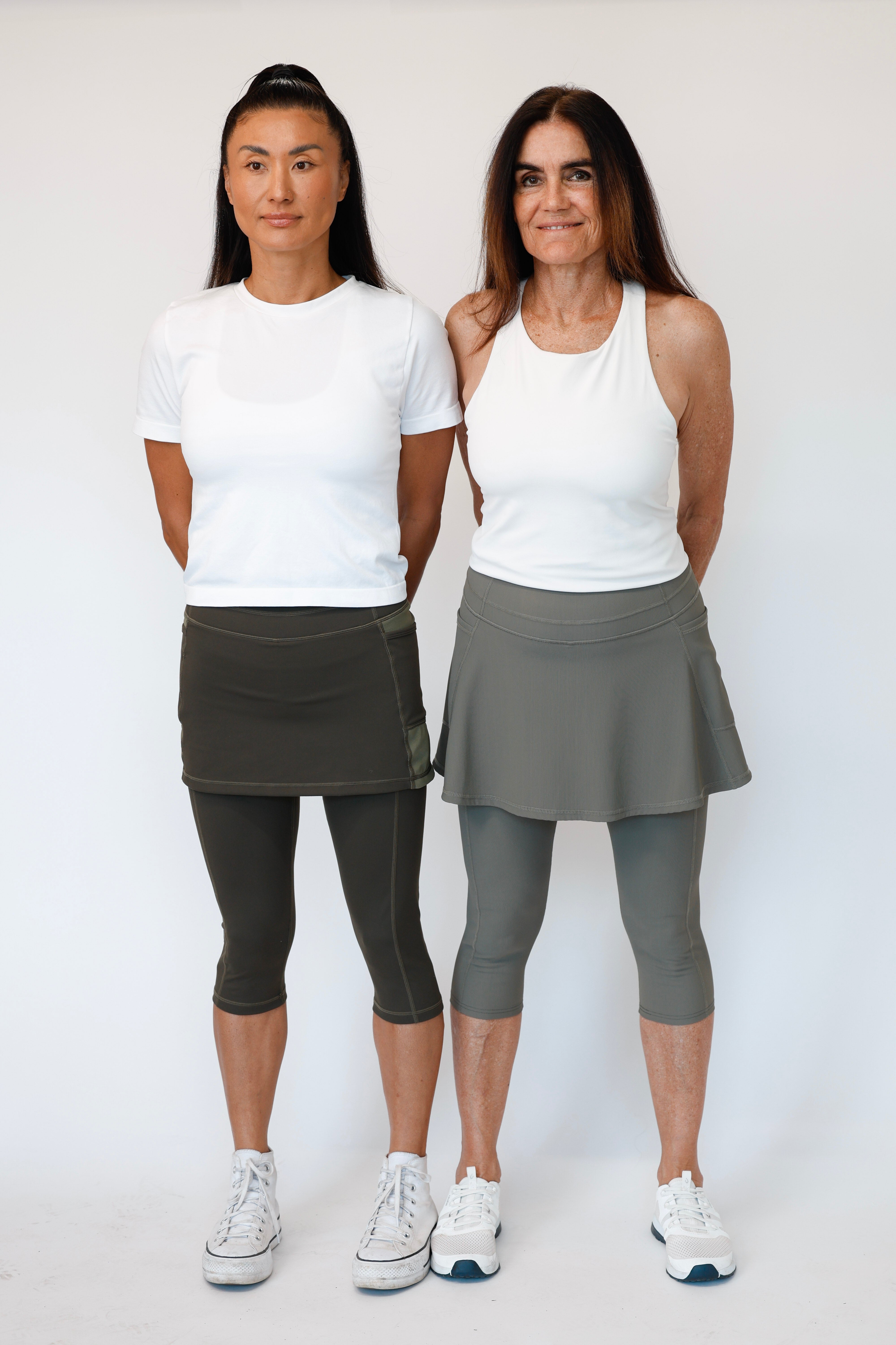 Two women wearing white tops and Olive skirted leggings standing side by side against a white background. Comfortable modest feminine active wear built for travel and built for movement; perfect for tennis, pickleball, golf, yoga, pilates and hiking. UPF sun protective and moisture wicking skirted leggings from a California based women founded and owned athletic wear company called Sol Sister Sport.