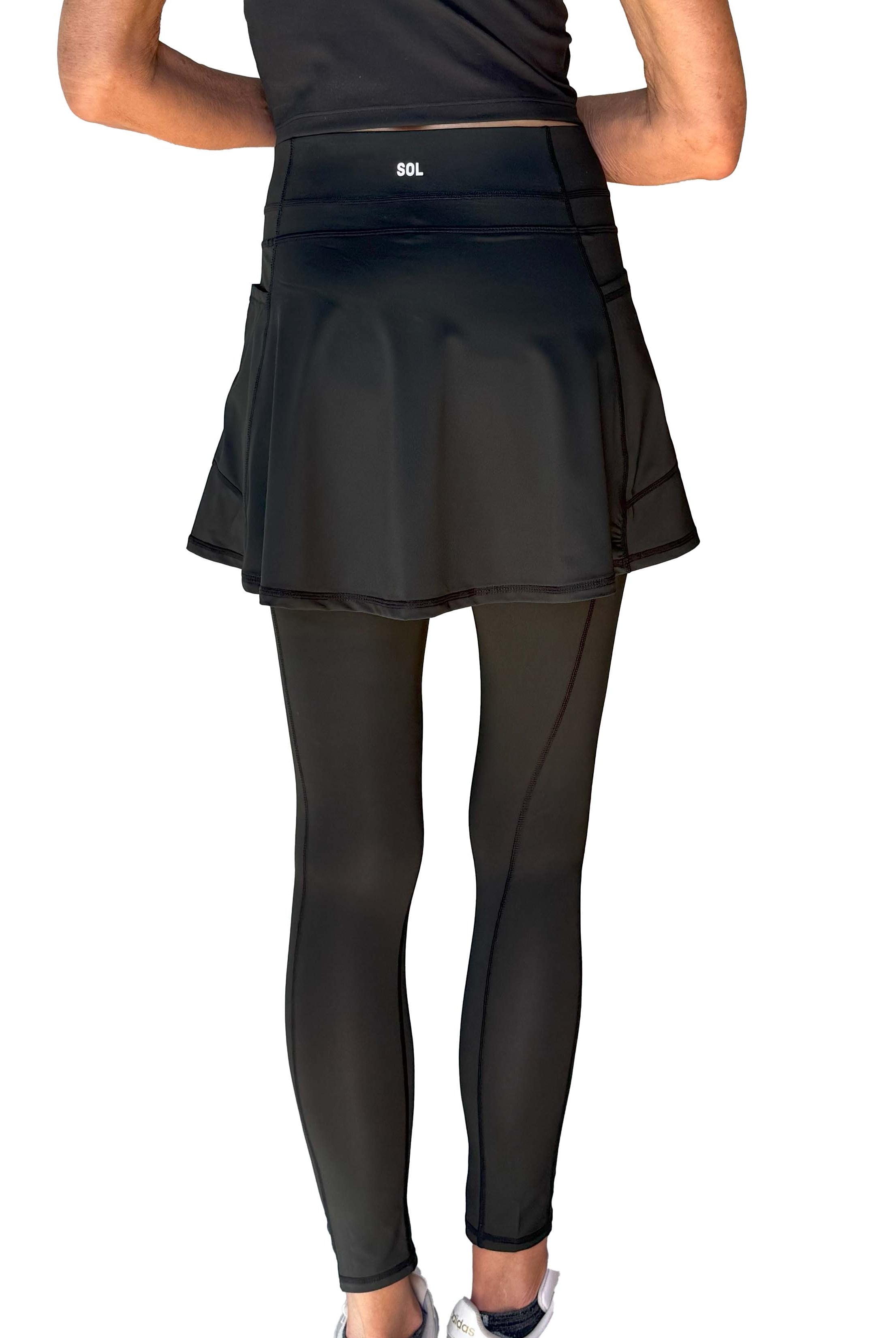 Person wearing a black athletic skirted leggings on a white background from behind