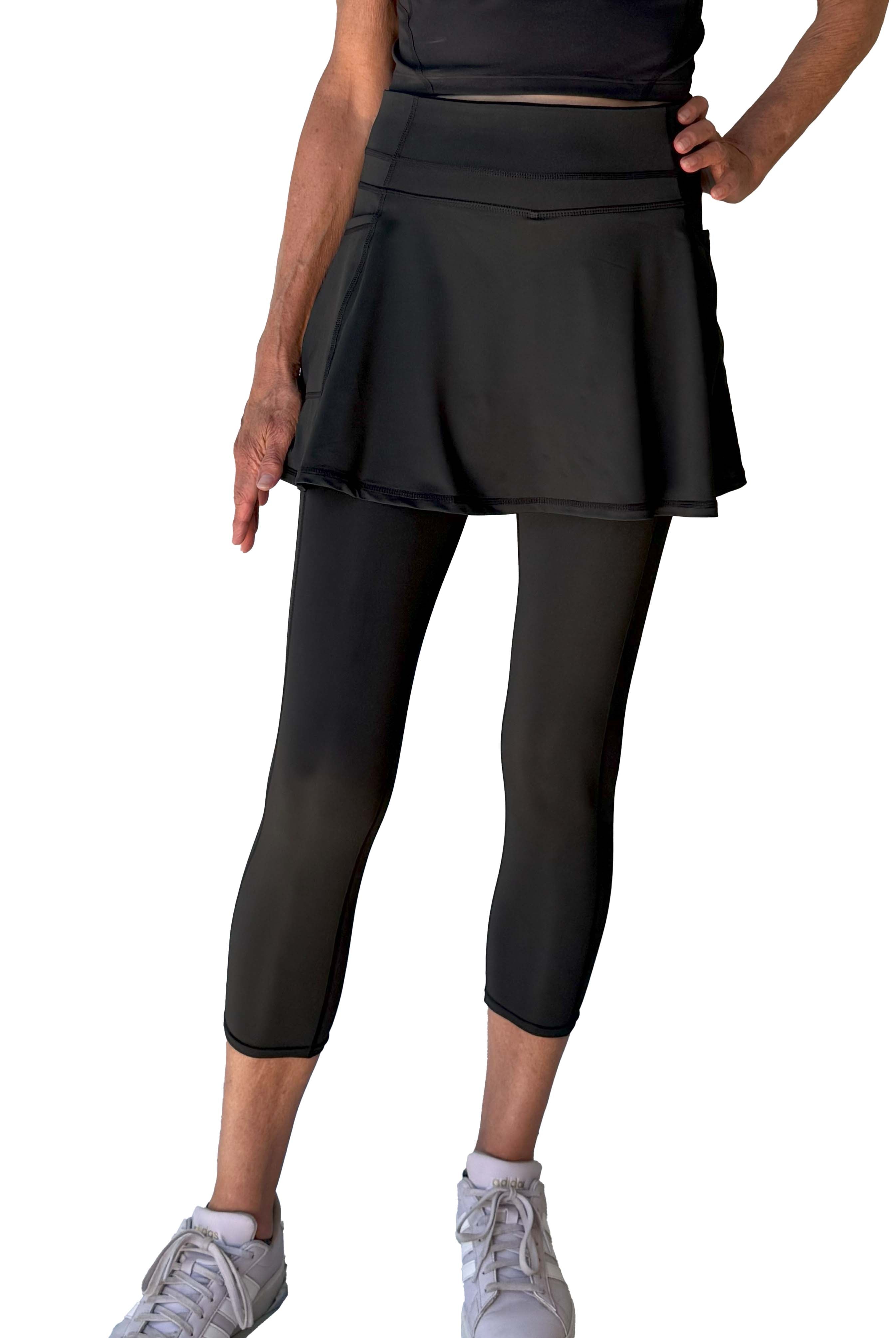 Person wearing a black athletic outfit with skirted midcalf leggings on a white background