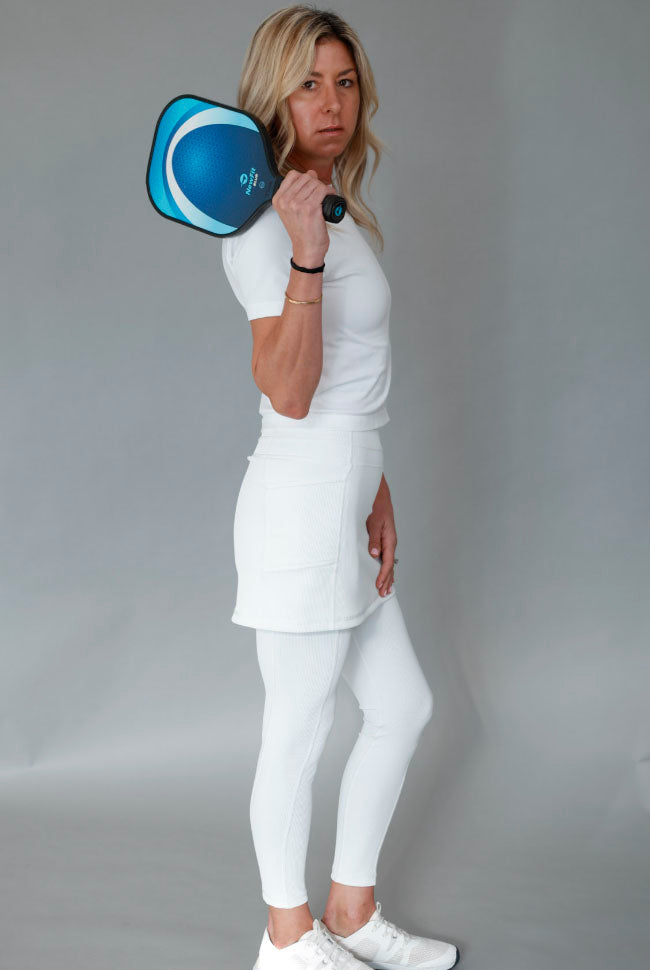 Person in white outfit holding a blue pickleball paddle against a gray background