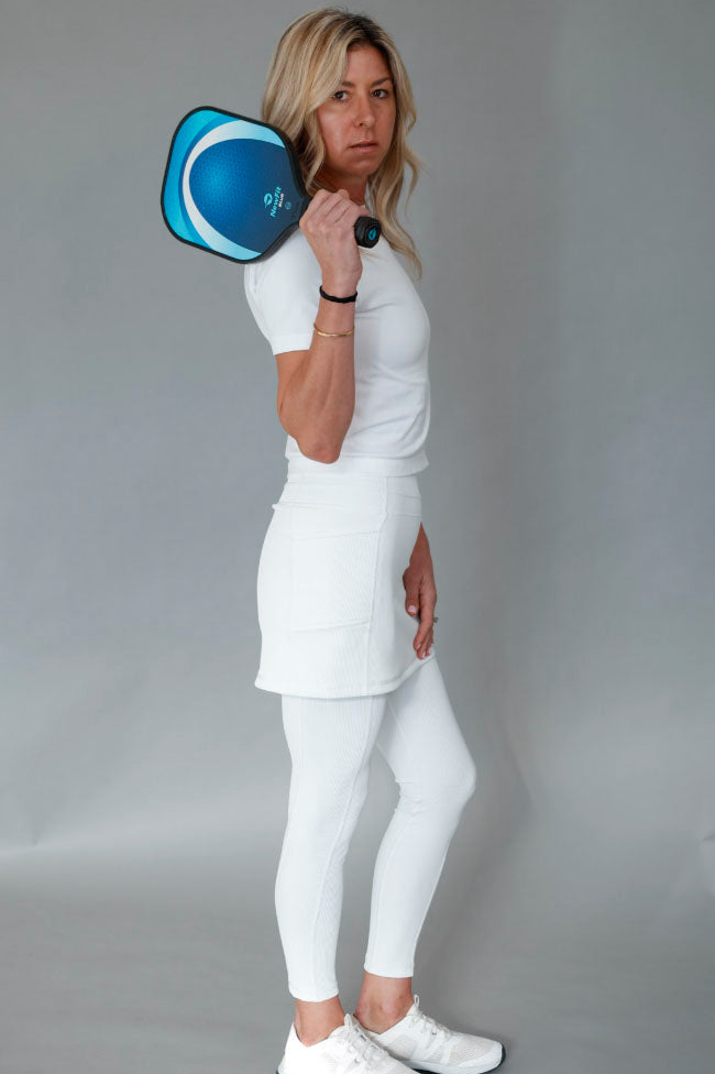 Person in white outfit holding a blue pickleball paddle against a gray background