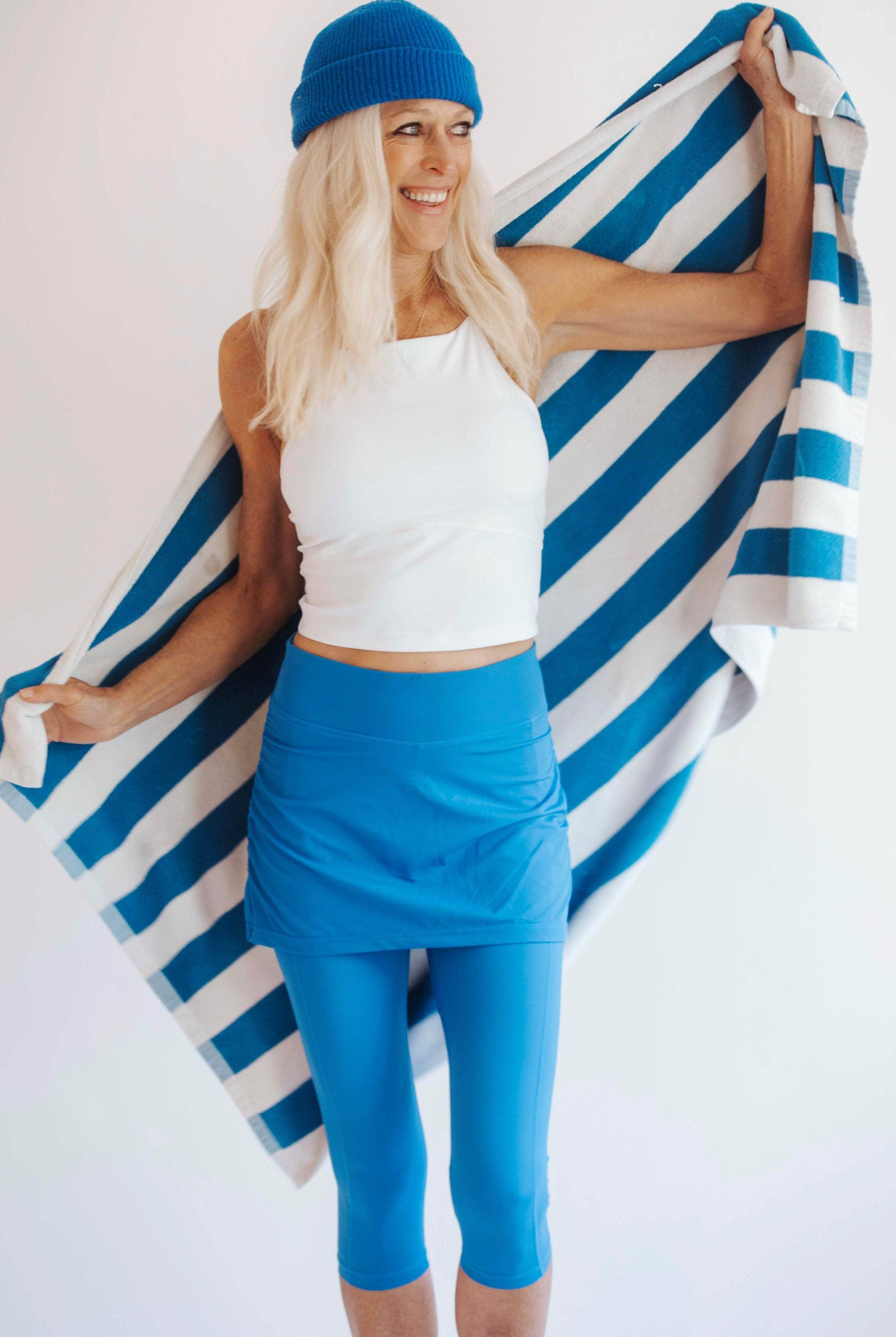 Smiling model is holding a blue and white beach towel while wearing a pretty bright blue swim skirted legging - water activity skirt.