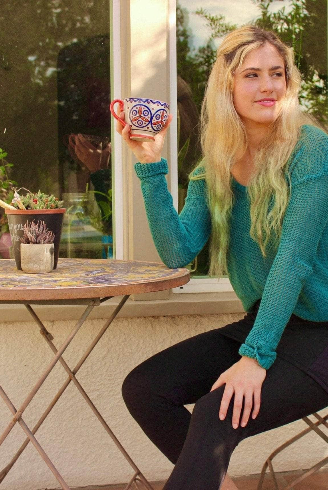 Skirted Mid-calf Length Leggings in Black. Model is sitting at cafe table with coffee cup in hand wearing a green sweater.