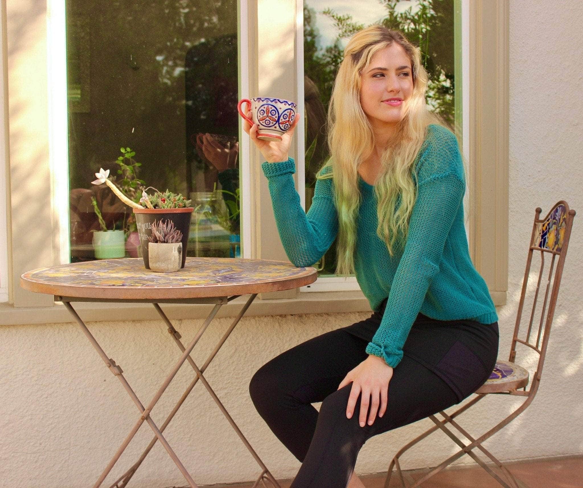 Skirted Mid-calf Length Leggings in Black. Model is sitting at cafe table with coffee cup in hand wearing a green sweater.