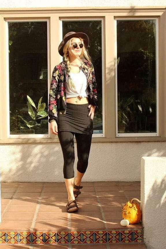 Skirted Mid-calf Length Leggings in Black worn by pretty and hip model with t-shirt tied in front and flowered cardigan.