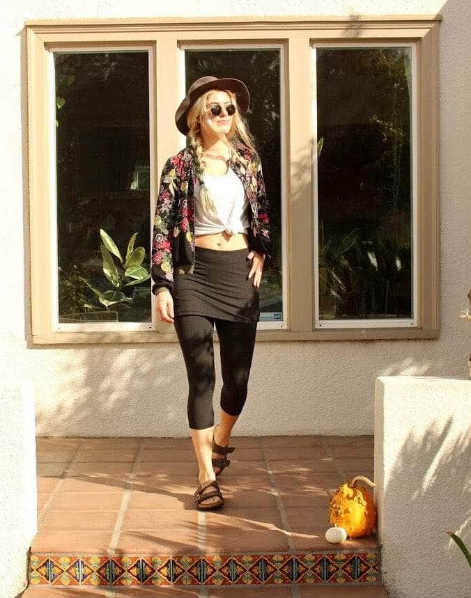 Skirted Mid-calf Length Leggings in Black worn by pretty and hip model with t-shirt tied in front and flowered cardigan.