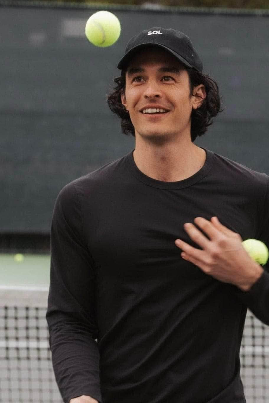 Black Sol Cap worn by handsome dark haired model juggling tennis balls - Sol Sister Sport