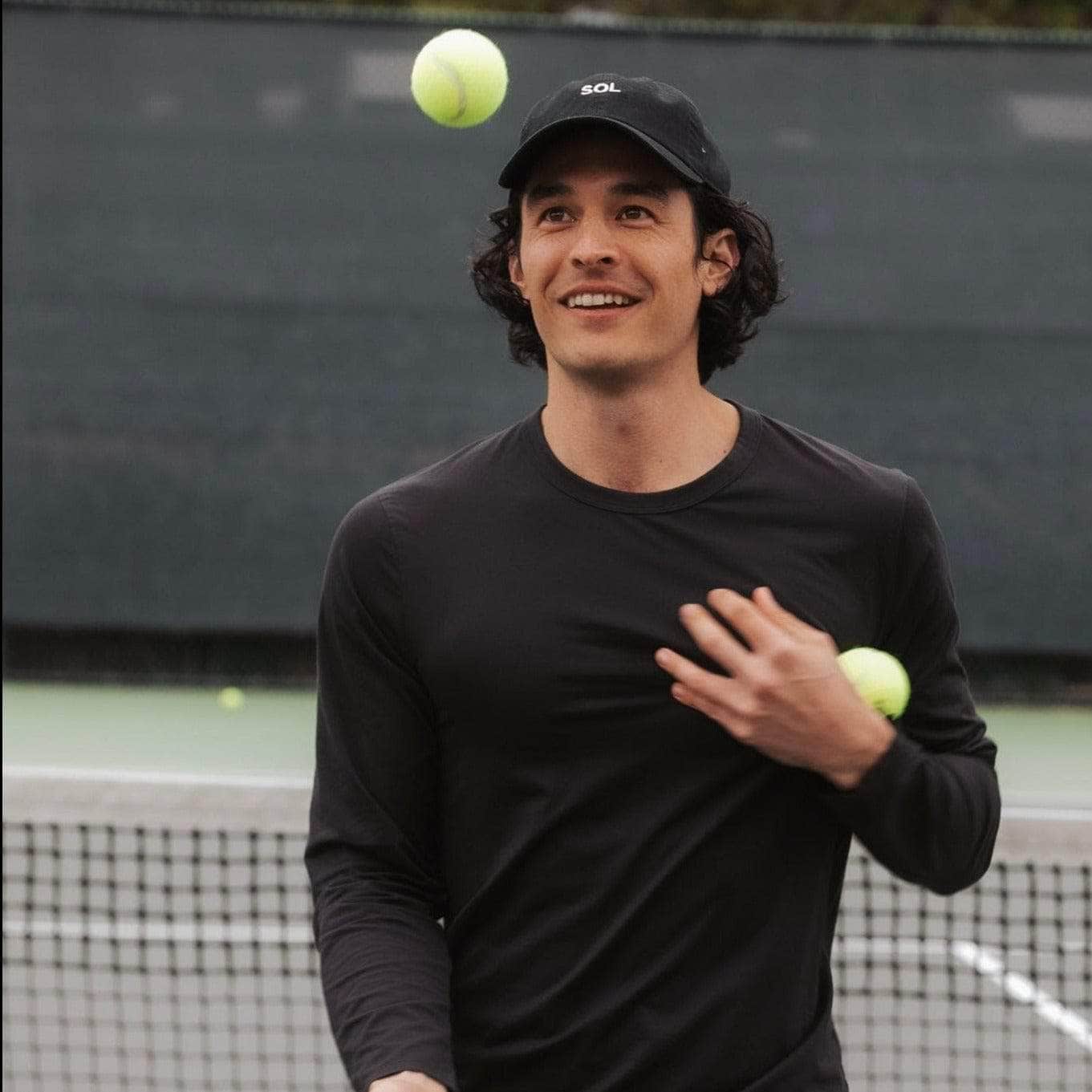 Black Sol Cap worn by handsome dark haired model juggling tennis balls - Sol Sister Sport