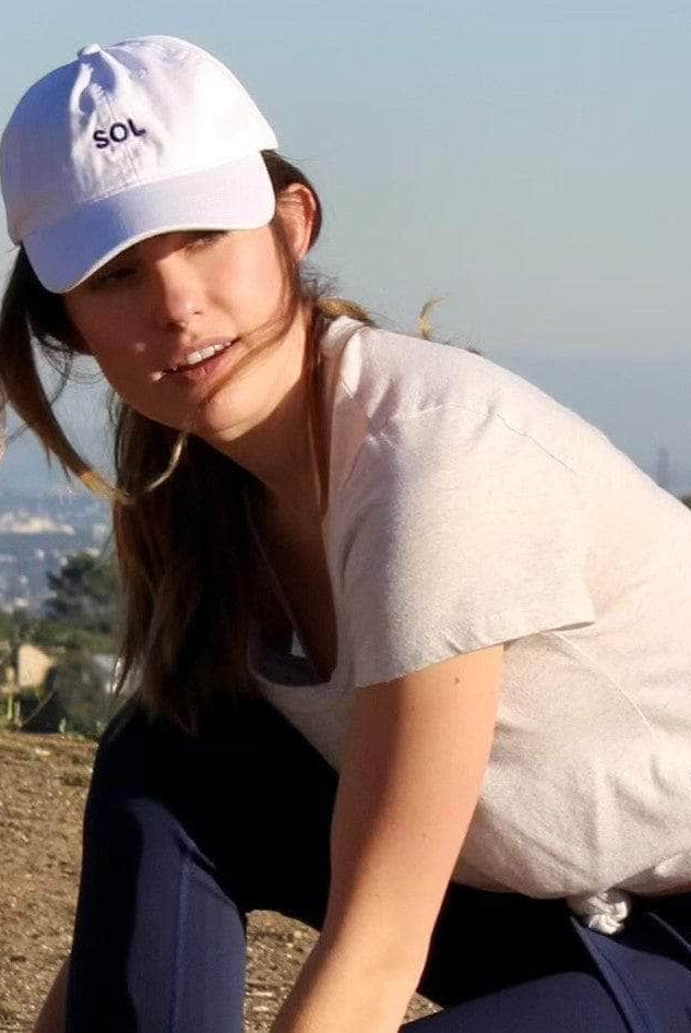 Model about to go for a run wearing a pretty White sports Cap with the letters SOL (for sun) on it.