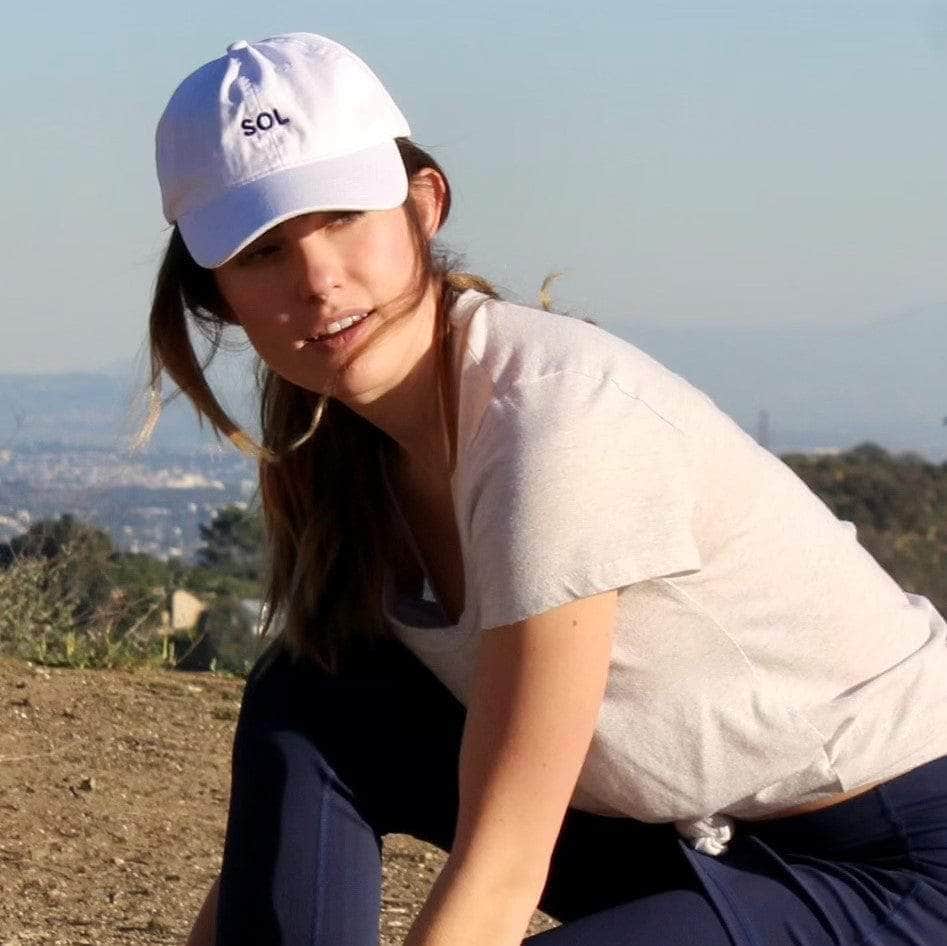Model about to go for a run wearing a pretty White sports Cap with the letters SOL (for sun) on it.