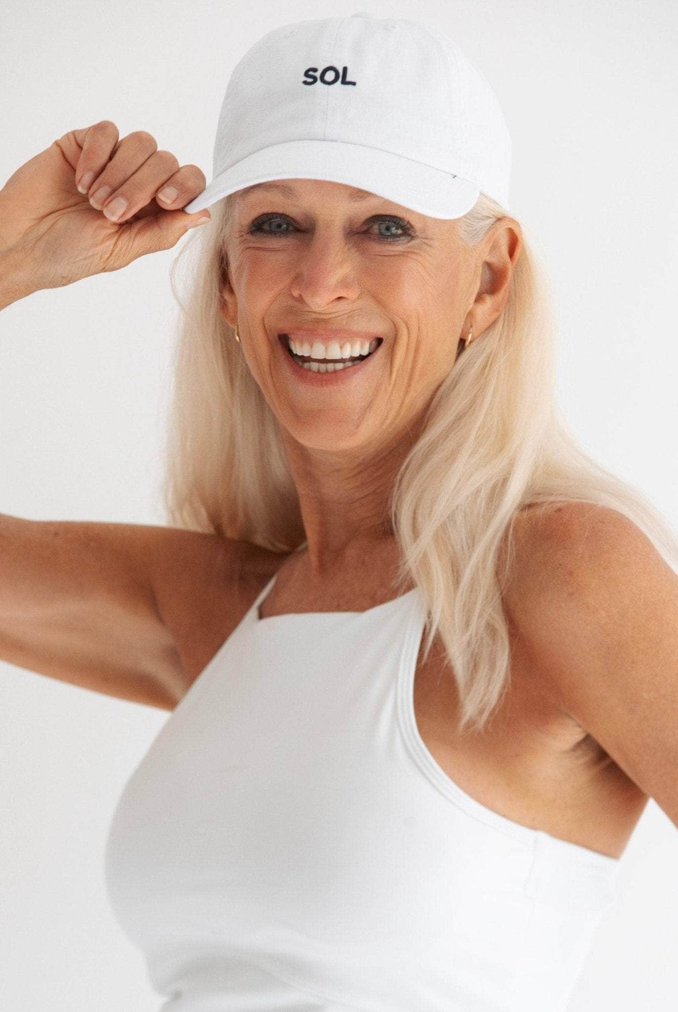 Pretty model wearing White sports Cap with the letters SOL (for sun) on it - Sol Sister Sport