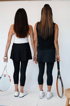 Two women standing back-to-back holding tennis rackets on a white background