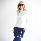 Smiling model wearing white lightweight athletic turtleneck top and blue and white skirted leggings.