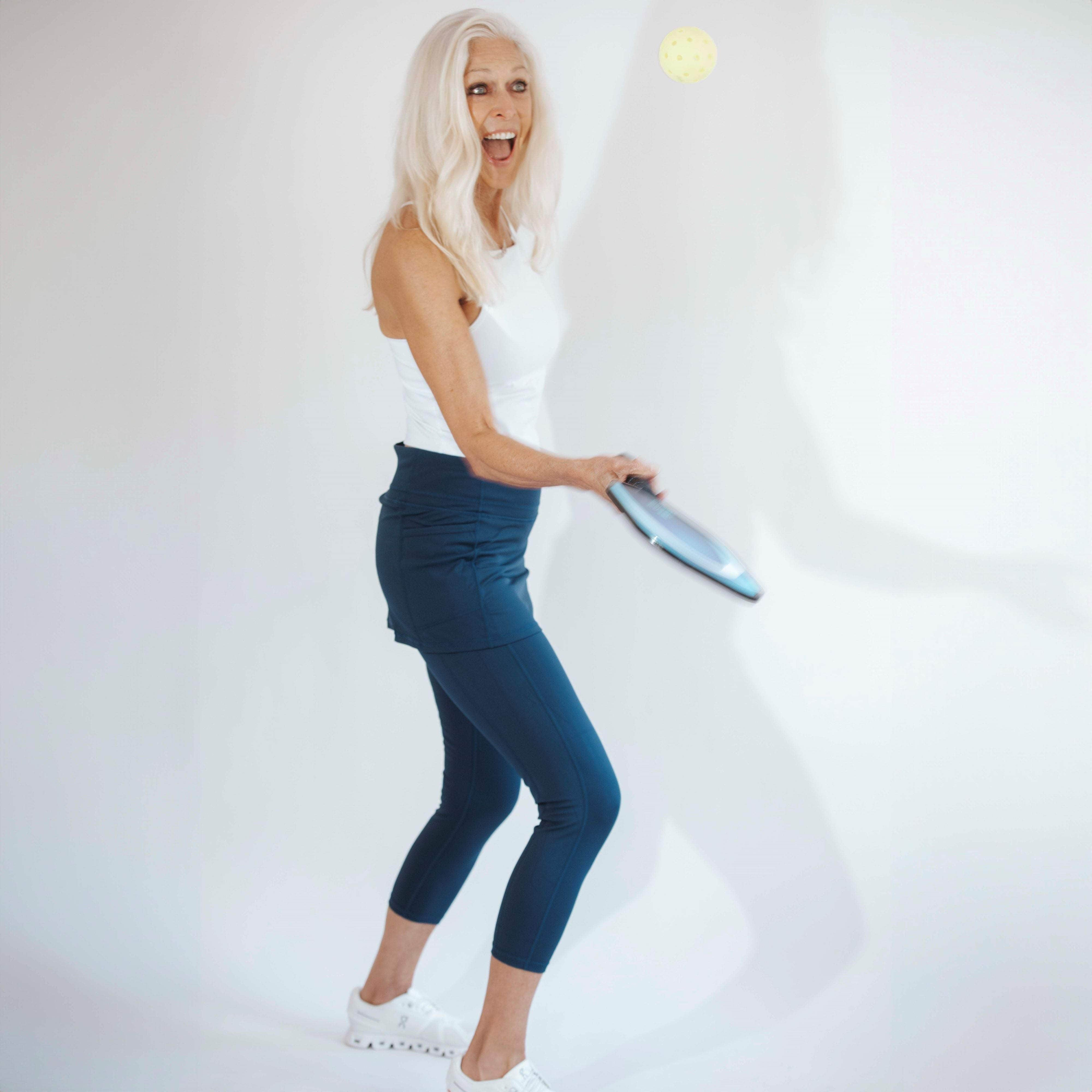 Silver haired model wearing blue colored skirted leggings with white athletic top.