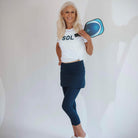 Beautiful silver haired model wearing navy blue skirted leggings holding a pickleball racket.