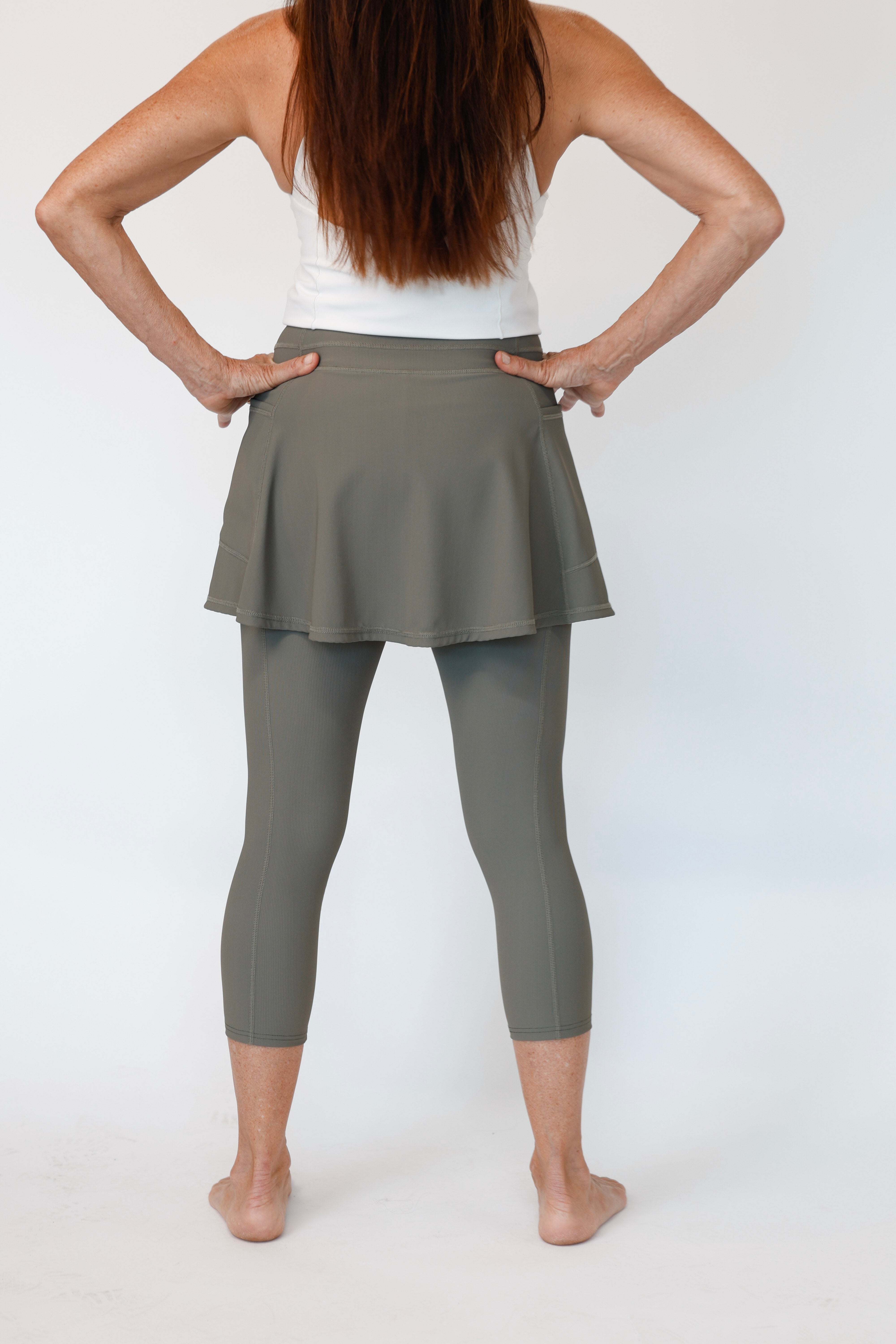 Woman standing and wearing Olive Khaki Ribbed Skirted leggings on a white background. Comfortable modest feminine active wear built for travel and built for movement; perfect for tennis, pickleball, golf, yoga, pilates and hiking. UPF sun protective and moisture wicking skirted leggings from a California based women founded and owned athletic wear company called Sol Sister Sport. 