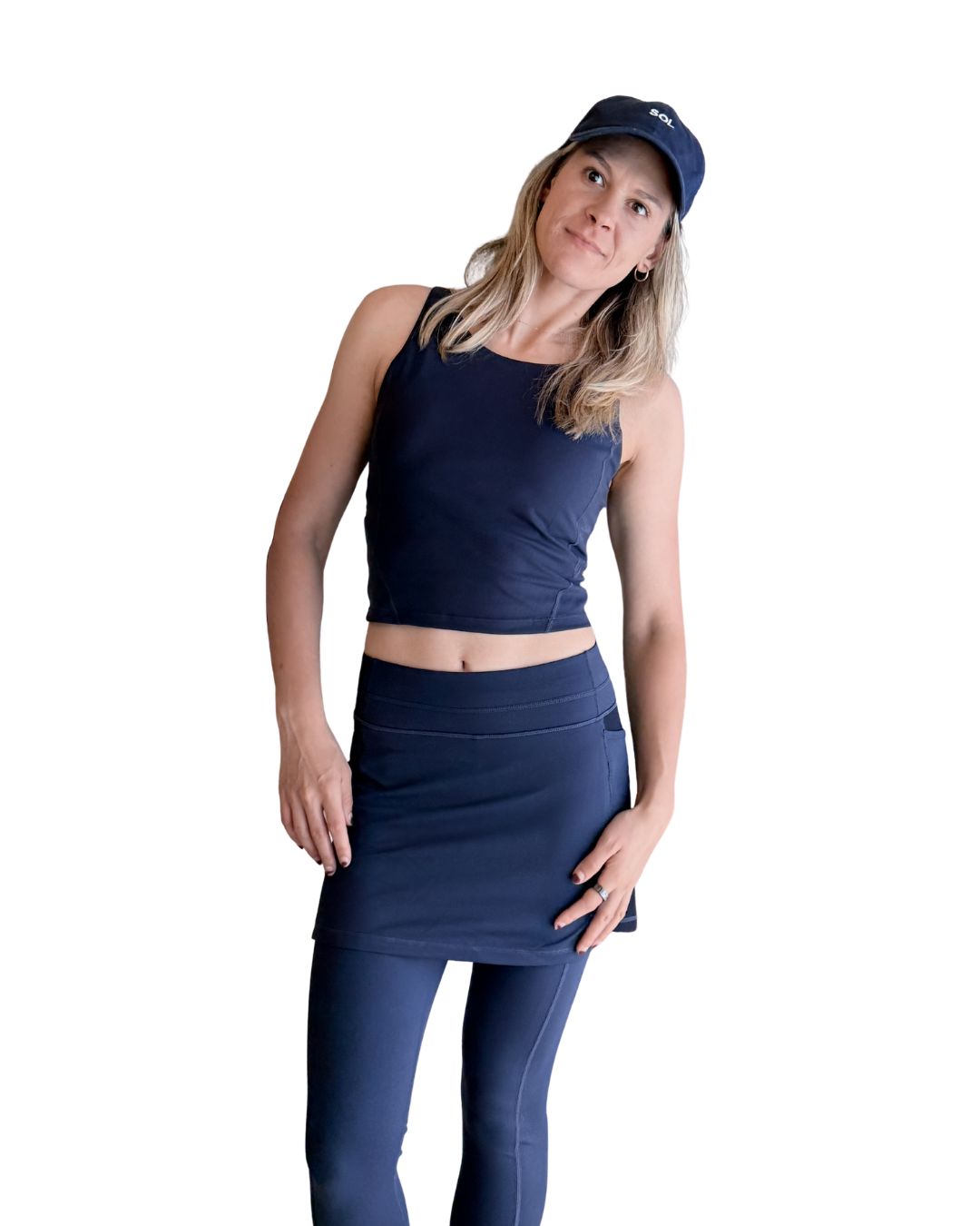 Woman wearing a navy athletic outfit with a skirt and cap on a white background