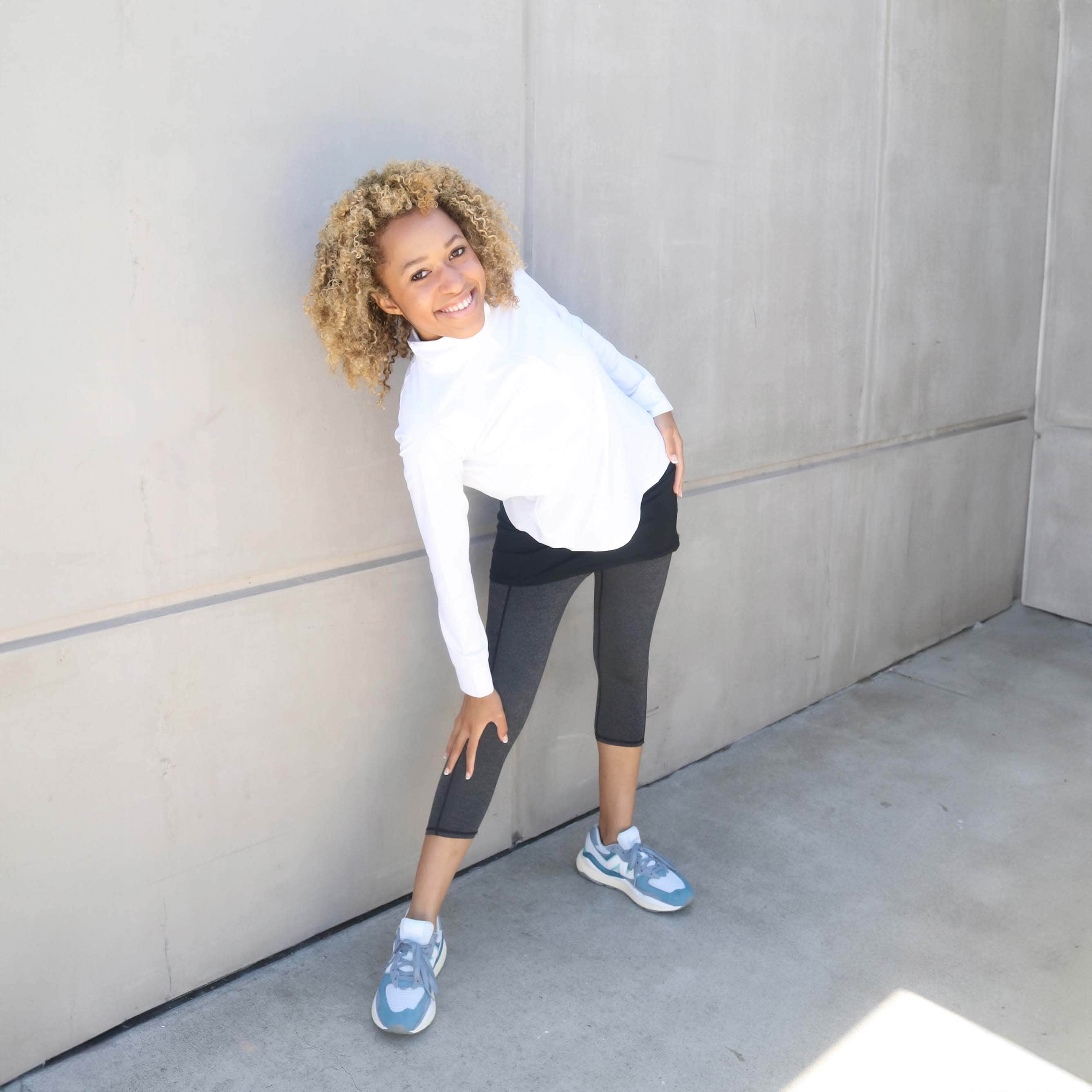 One piece black skirt with heather grey capris length leggings.  Model is standing near a building leaning onto her knee wearing white zip front activewear shirt.