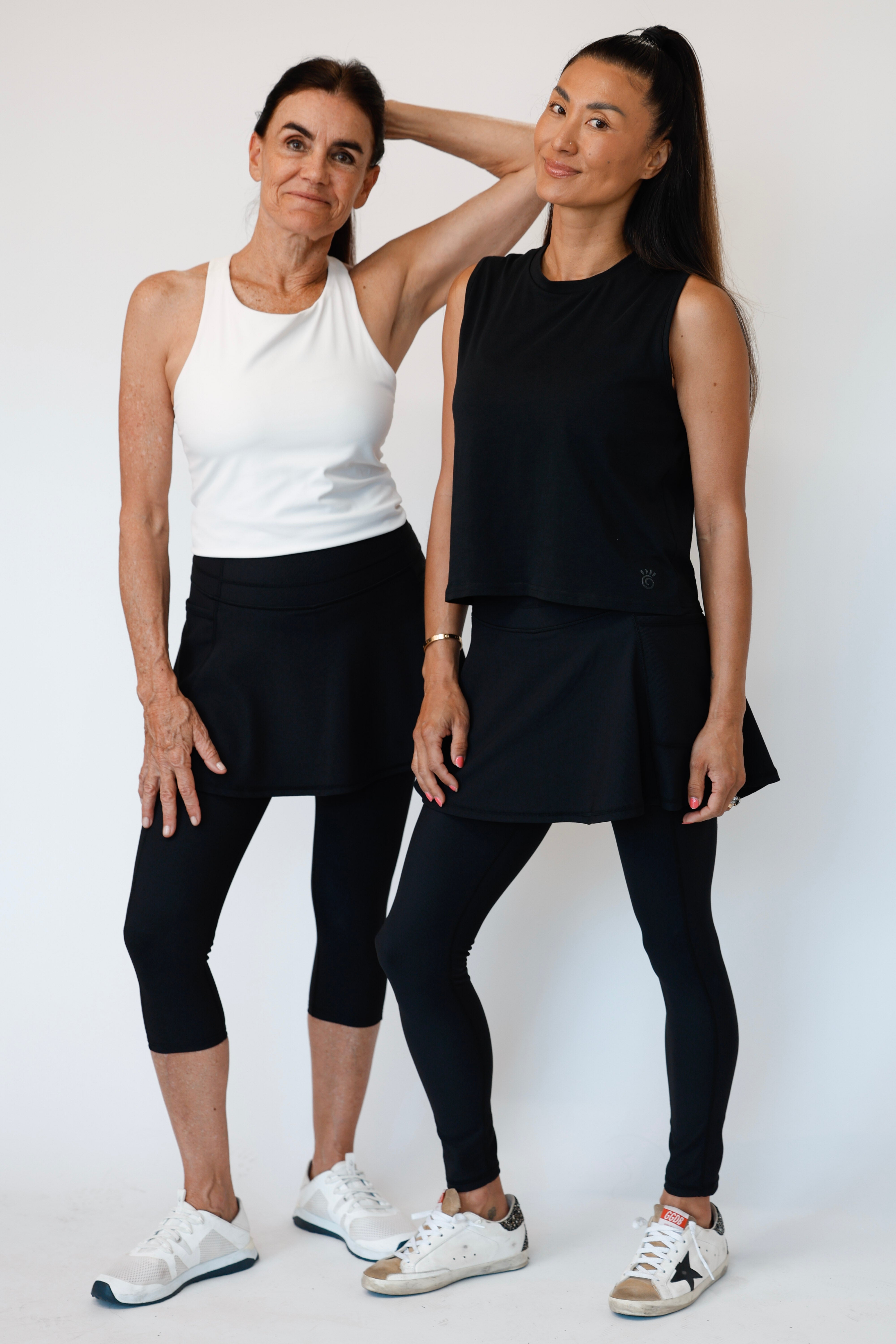 Two women wearing matching black flare ribbed skirted leggings and white athletic outfits against a white background. 
Comfortable modest feminine active wear built for travel and built for movement; perfect for tennis, pickleball, golf, yoga, pilates and hiking. UPF sun protective and moisture wicking skirted leggings from a California based women founded and owned athletic wear company called Sol Sister Sport. 