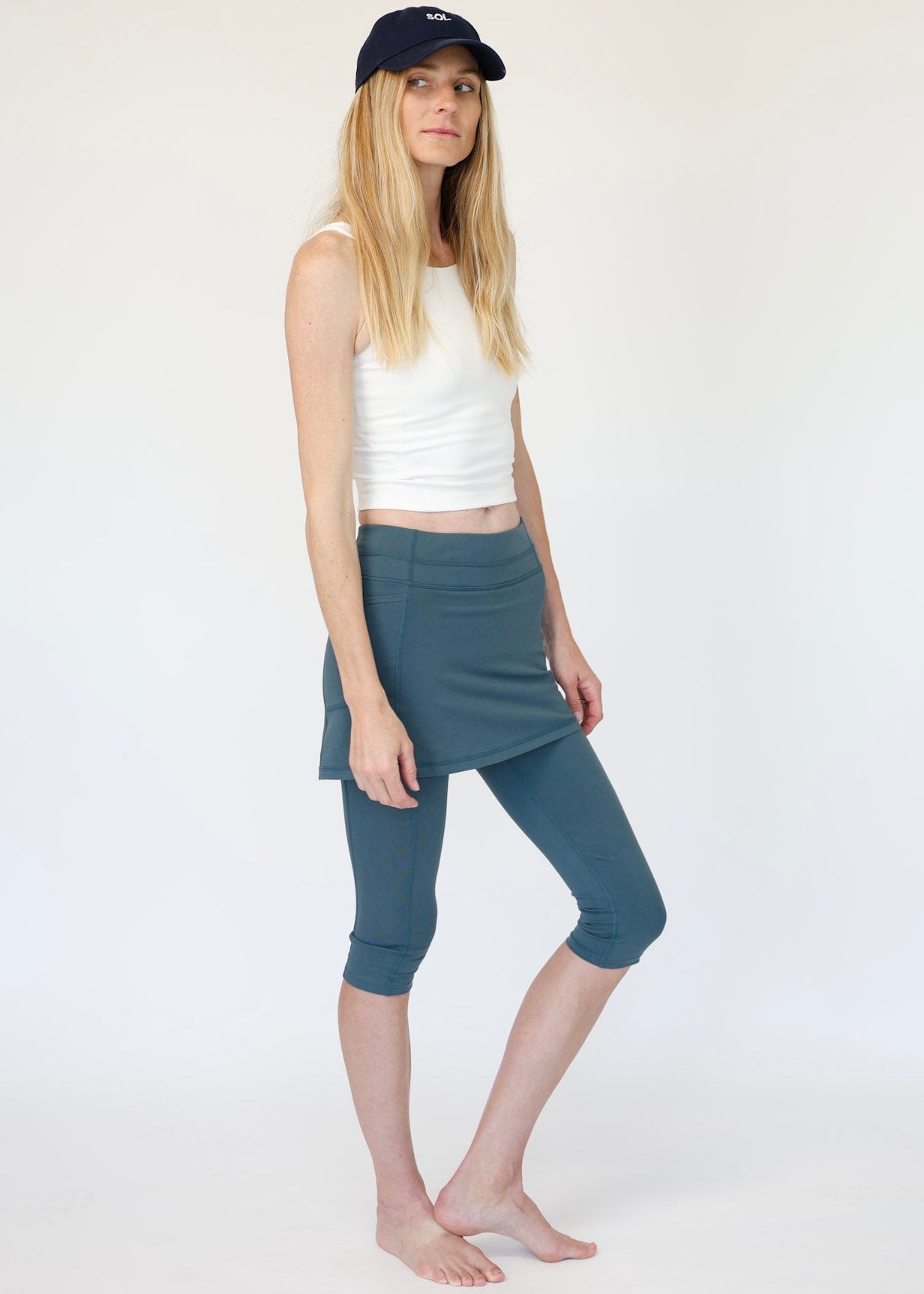 Woman wearing a white tank top and blue capri pants on a white background
