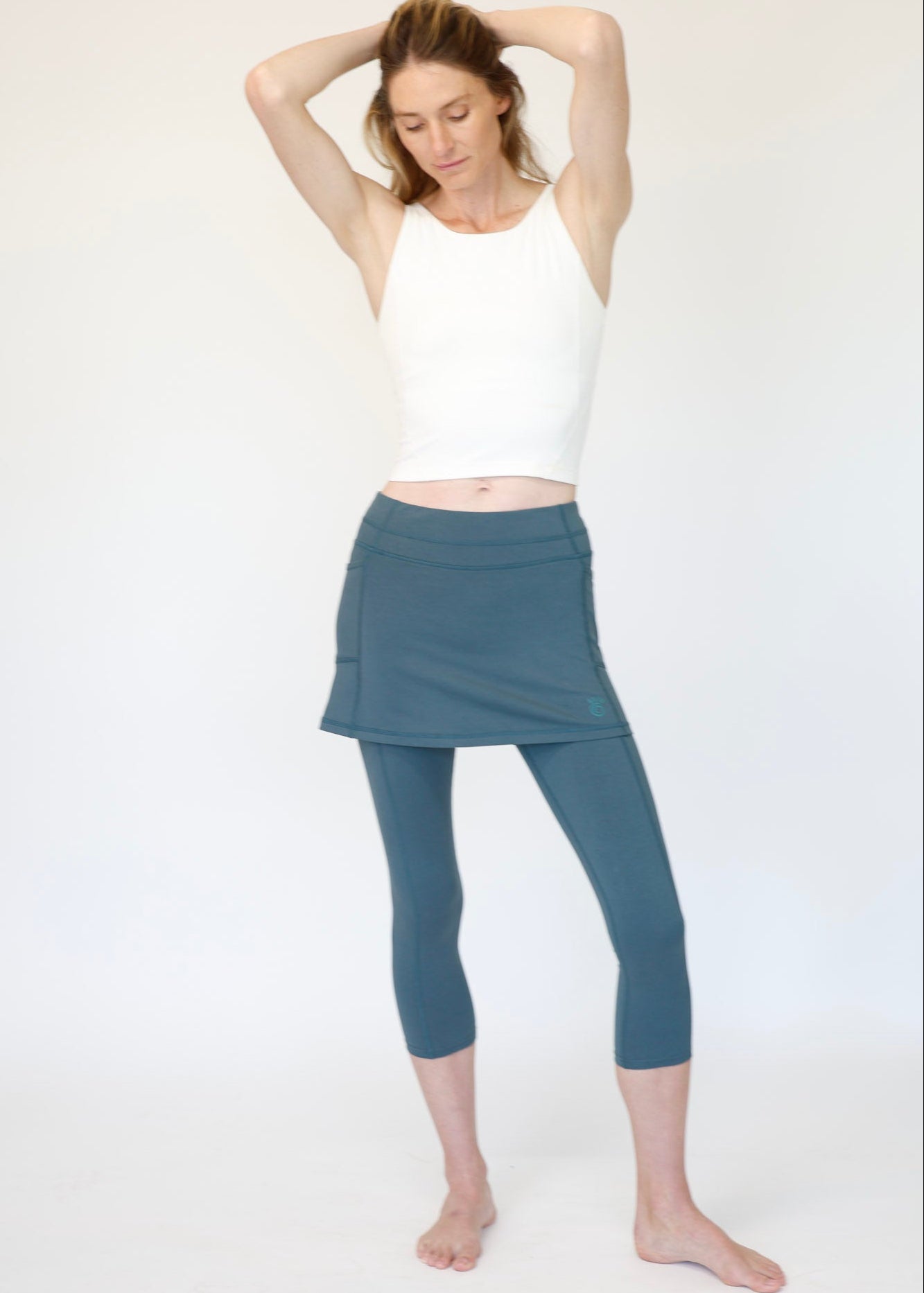 Woman wearing a white tank top and blue skirted leggings on a white background