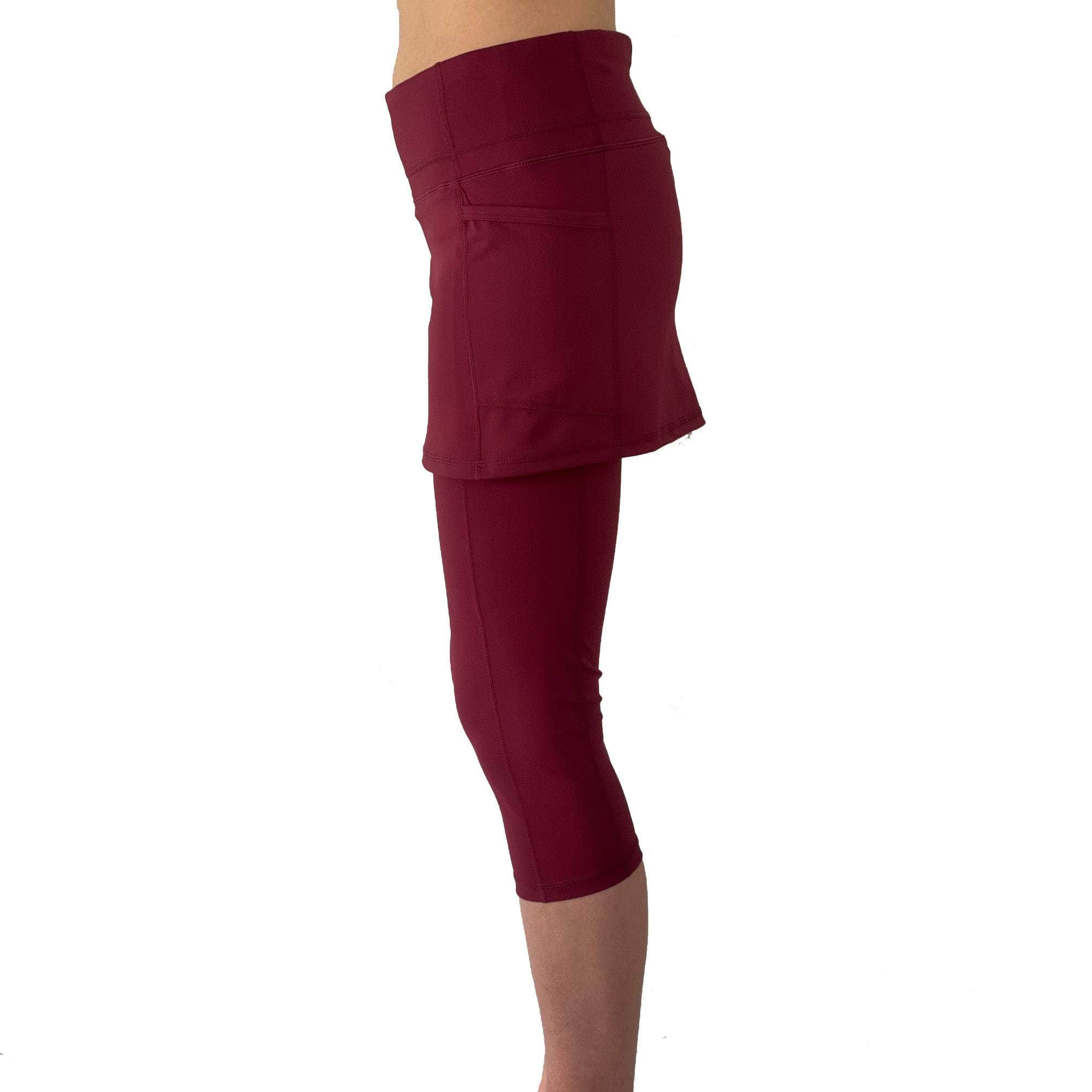 Studio shot of model from waist down wearing capris length cranberry colored skirted leggings, side view.