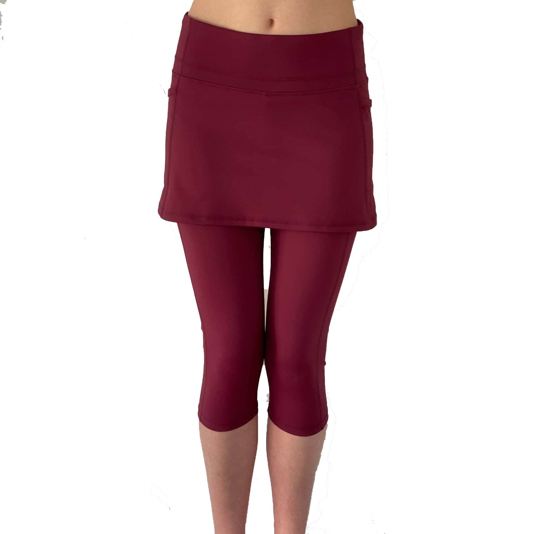 Studio shot of model from waist down wearing capris length cranberry colored skirted leggings, front view.