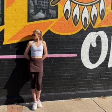 Shot of model in front of wall mural outdoors wearing Espresso Brown 2-1 Skirted Ankle-Length Leggings from front