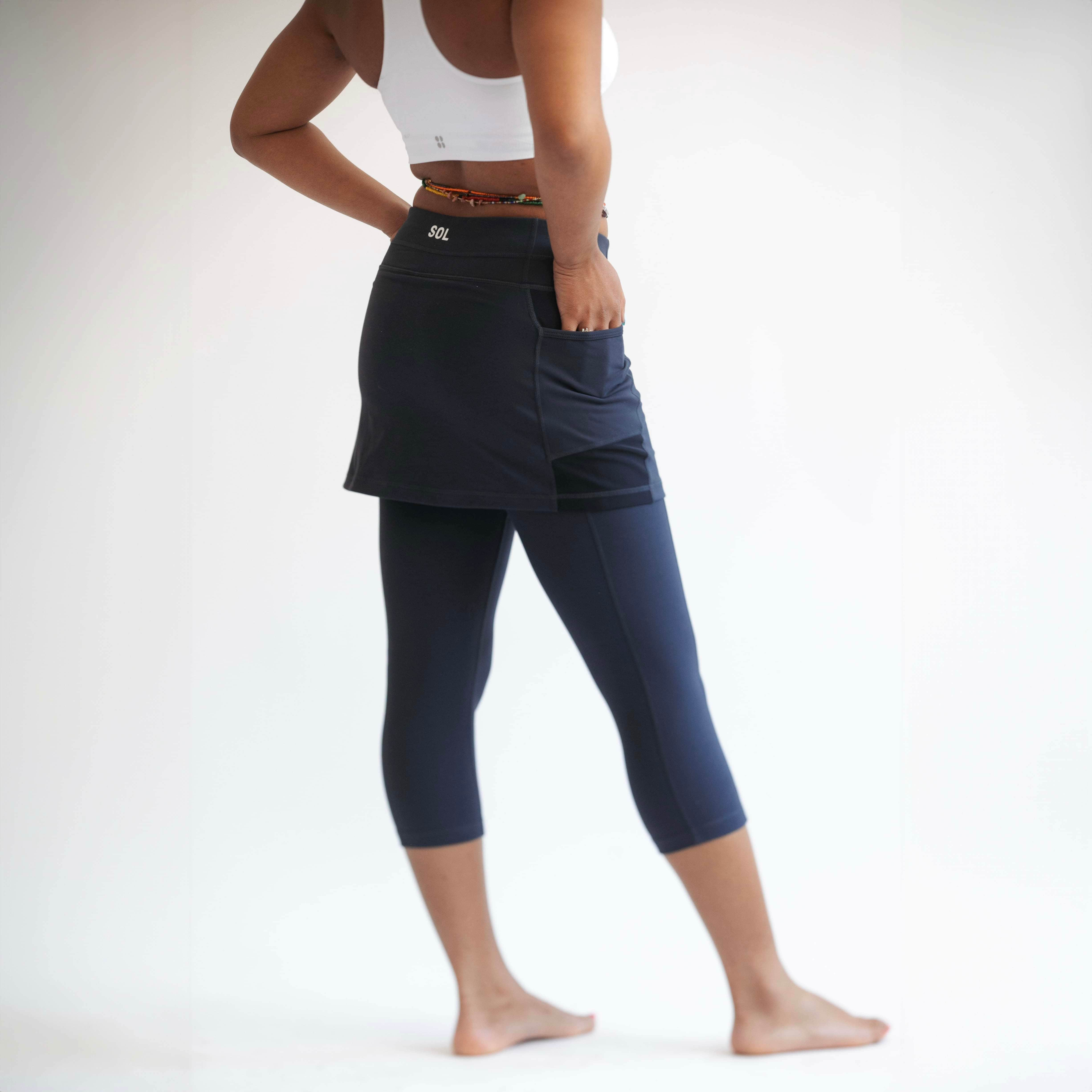 Rear shot of model wearing midnight dark blue leggings with attached skirt and white sports bra on top..