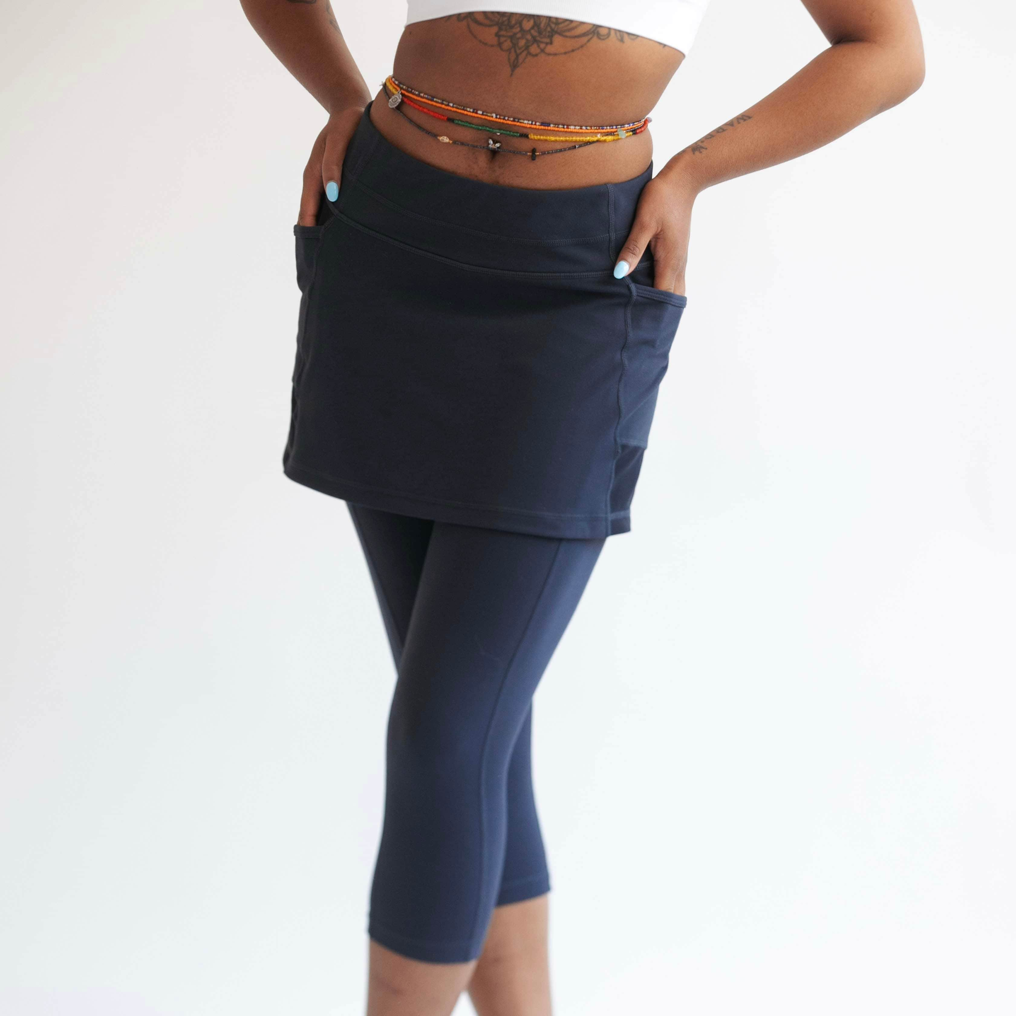 Close up studio shot of model wearing dark blue capris length leggings with attached skirt.