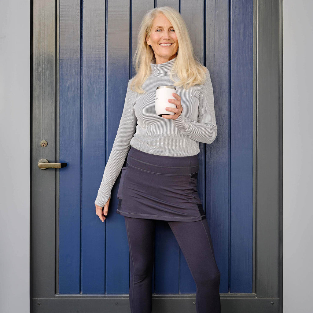Blonde woman wearing dark blue skirted leggings in front of blue door holding a cup of coffee