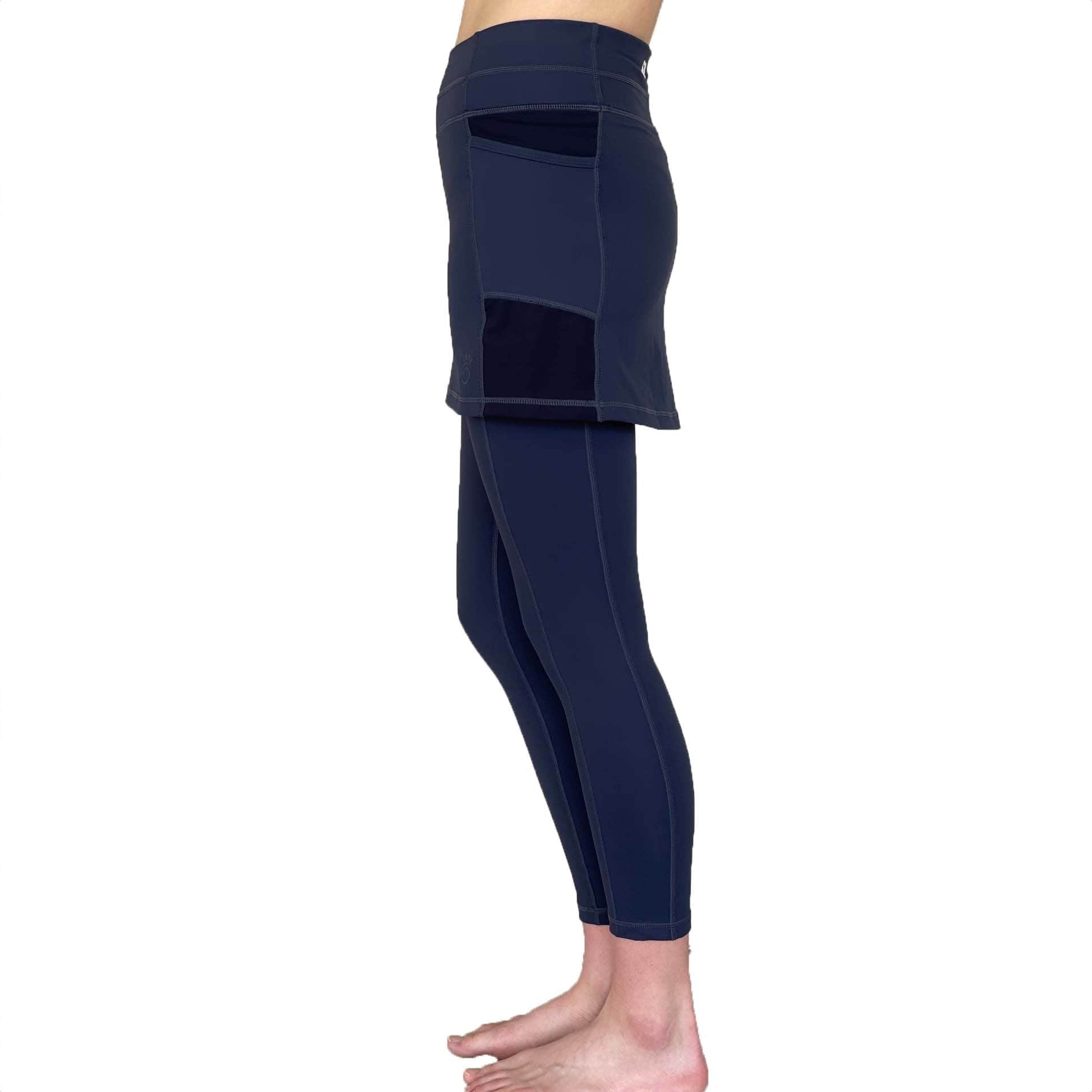 Woman wearing dark blue 7/8th legging length skirted leggings from waist down with white background from side view.